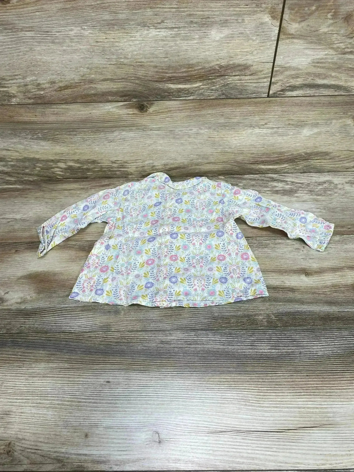 Flat lay of H&M baby long-sleeve floral top size 6-9 months showing pastel floral print and scalloped cuffs on wood background