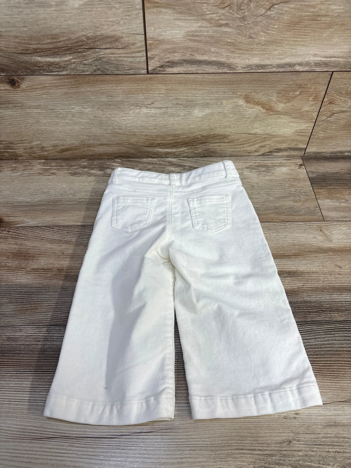 Back view of white Janie & Jack wide-leg corduroy toddler pants showing back pockets and cropped wide legs on wooden floor