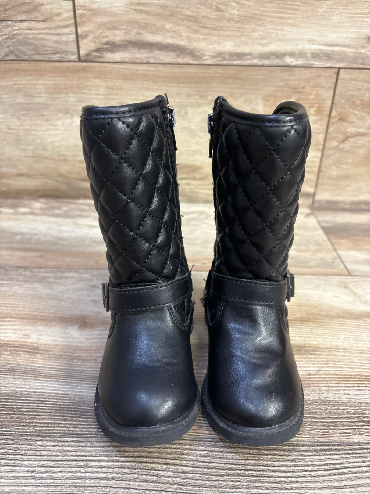 Front view of Clares quilted black riding boots with diamond shaft, ankle buckle and side zipper on wood floor