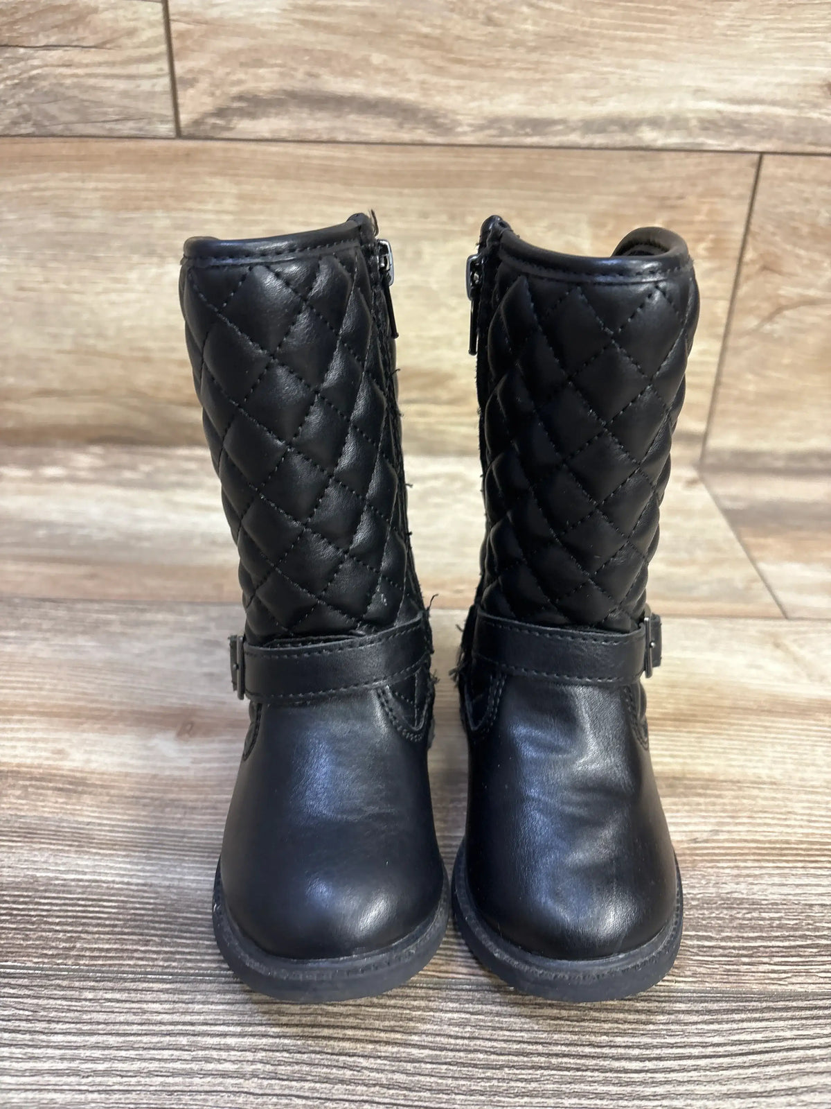 Front view of Clares quilted black riding boots with diamond shaft, ankle buckle and side zipper on wood floor