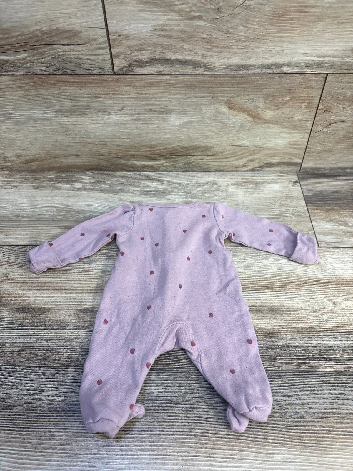 Front view of a purple Carter’s sleeper in size Preemie, showcasing strawberry pattern and footed legs on a wood-look floor