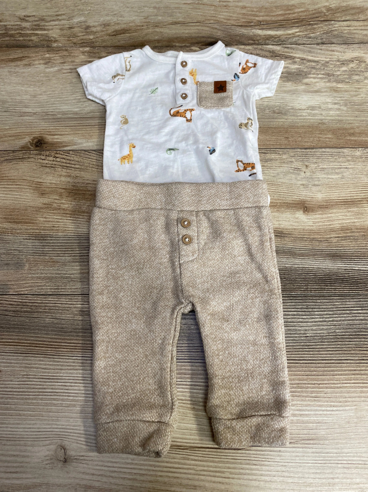 Baby outfit with animal print short-sleeve top and beige knit pants on wood background
