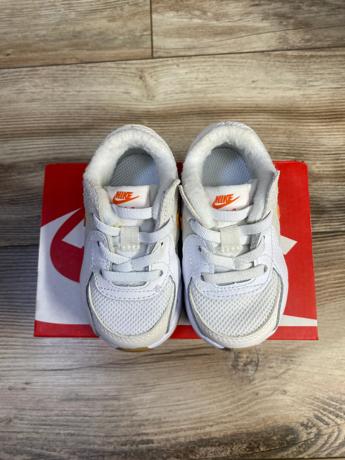 Top view of Nike Air Max Excee TD sneakers in white with orange accents on a red Nike shoebox