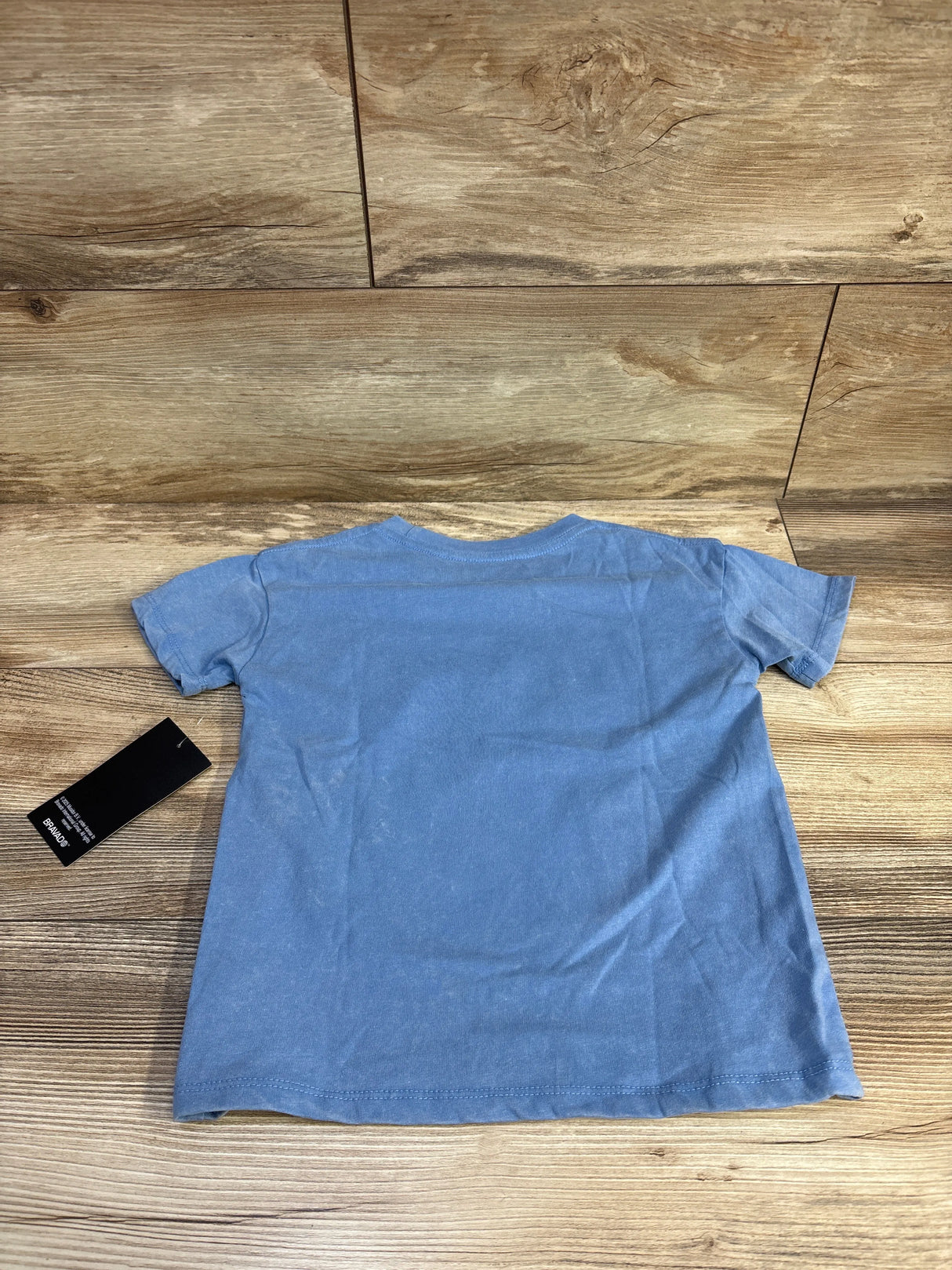 Back view of blue Rolling Stones toddler T-shirt (size 5T) showing short sleeves and attached tag on wood floor background