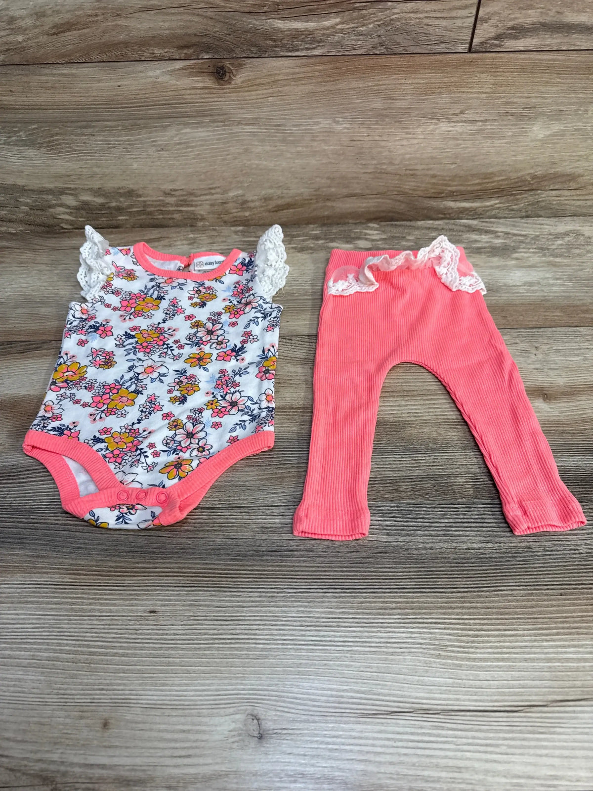 Flat lay of Daisy Fuentes 2-piece floral bodysuit and coral ribbed leggings showing lace ruffle sleeves on wood background