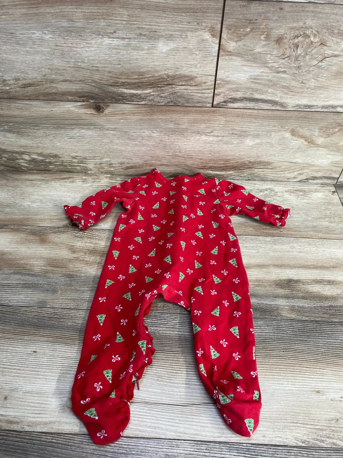 Red Christmas baby onesie with green trees and white bows, laid on wood floor