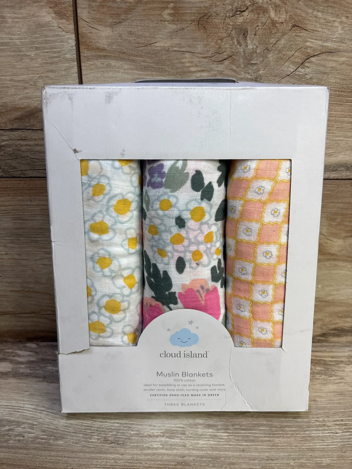 Front view of Cloud Island 3-pack muslin swaddle blankets showing three floral and geometric prints in a white display box on a wooden surface