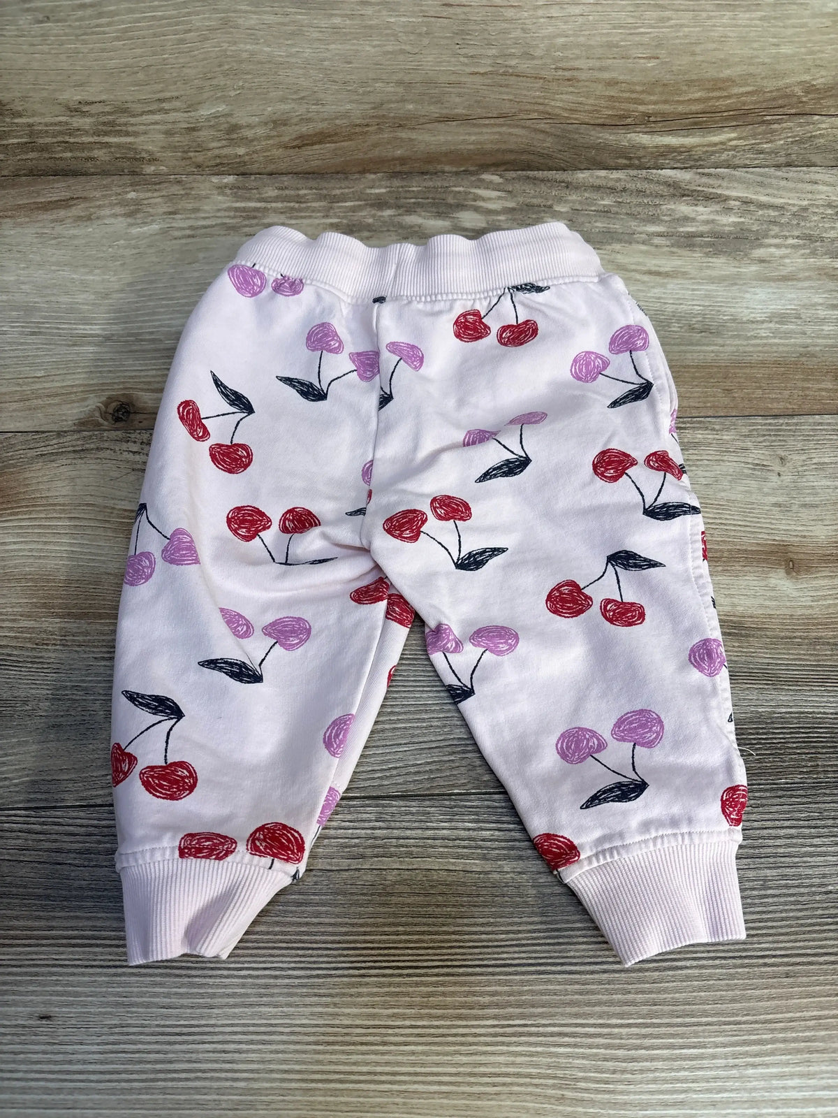 Baby pink jogger pants with red and purple cherry print, displayed on wood surface