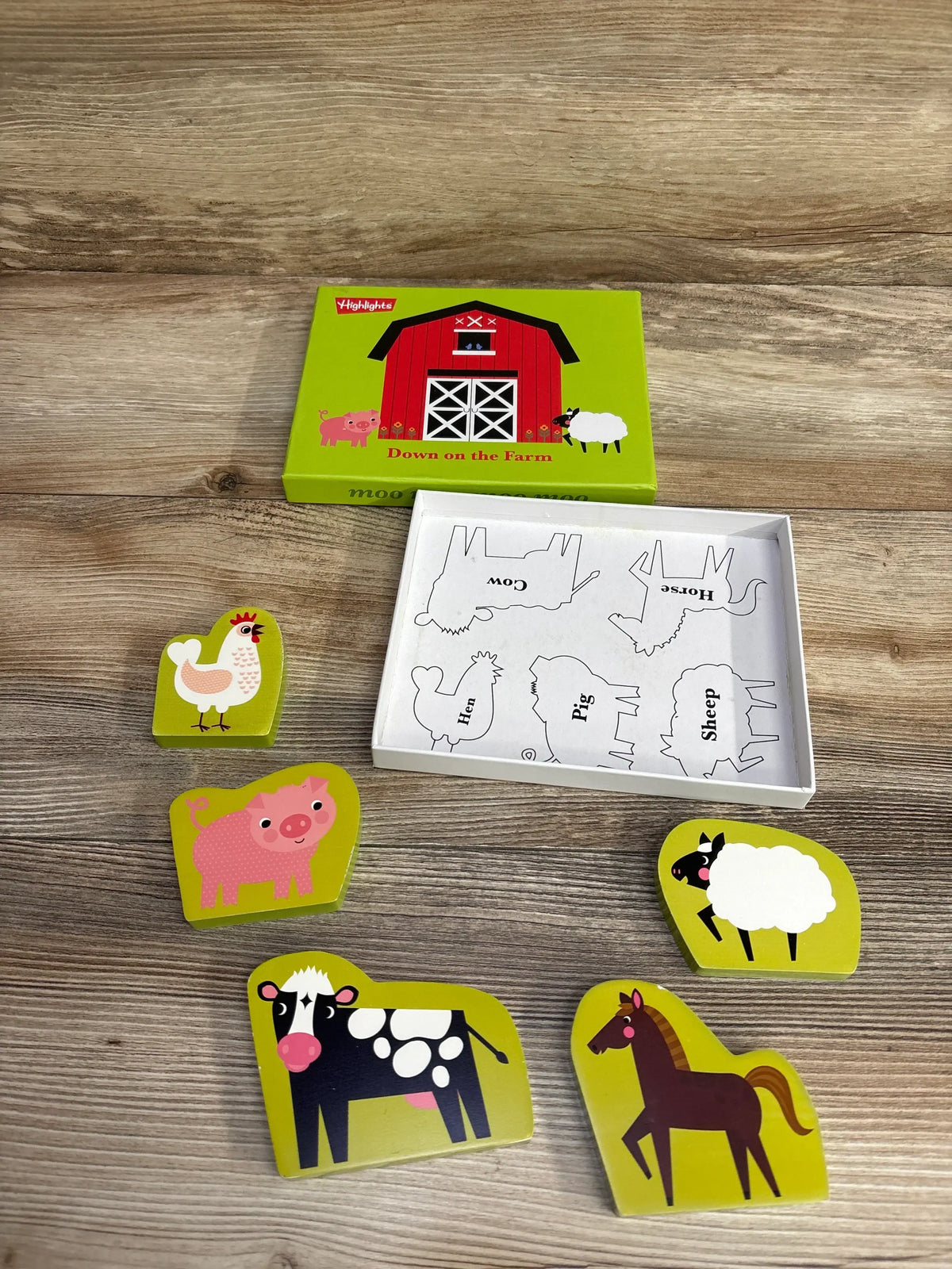 Children's farm animal wooden puzzle pieces including hen, pig, cow, sheep, horse with barn box on wood surface