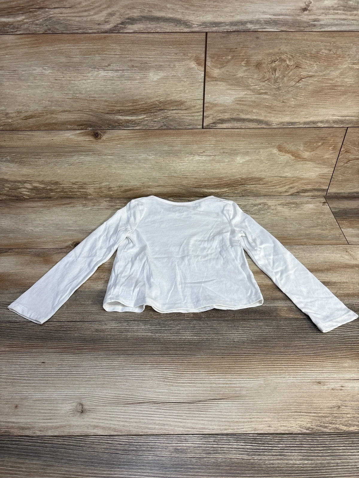 Back view of Max Studio white toddler long-sleeve shirt (size 4T) showing plain back and wavy hem laid flat on wood floor