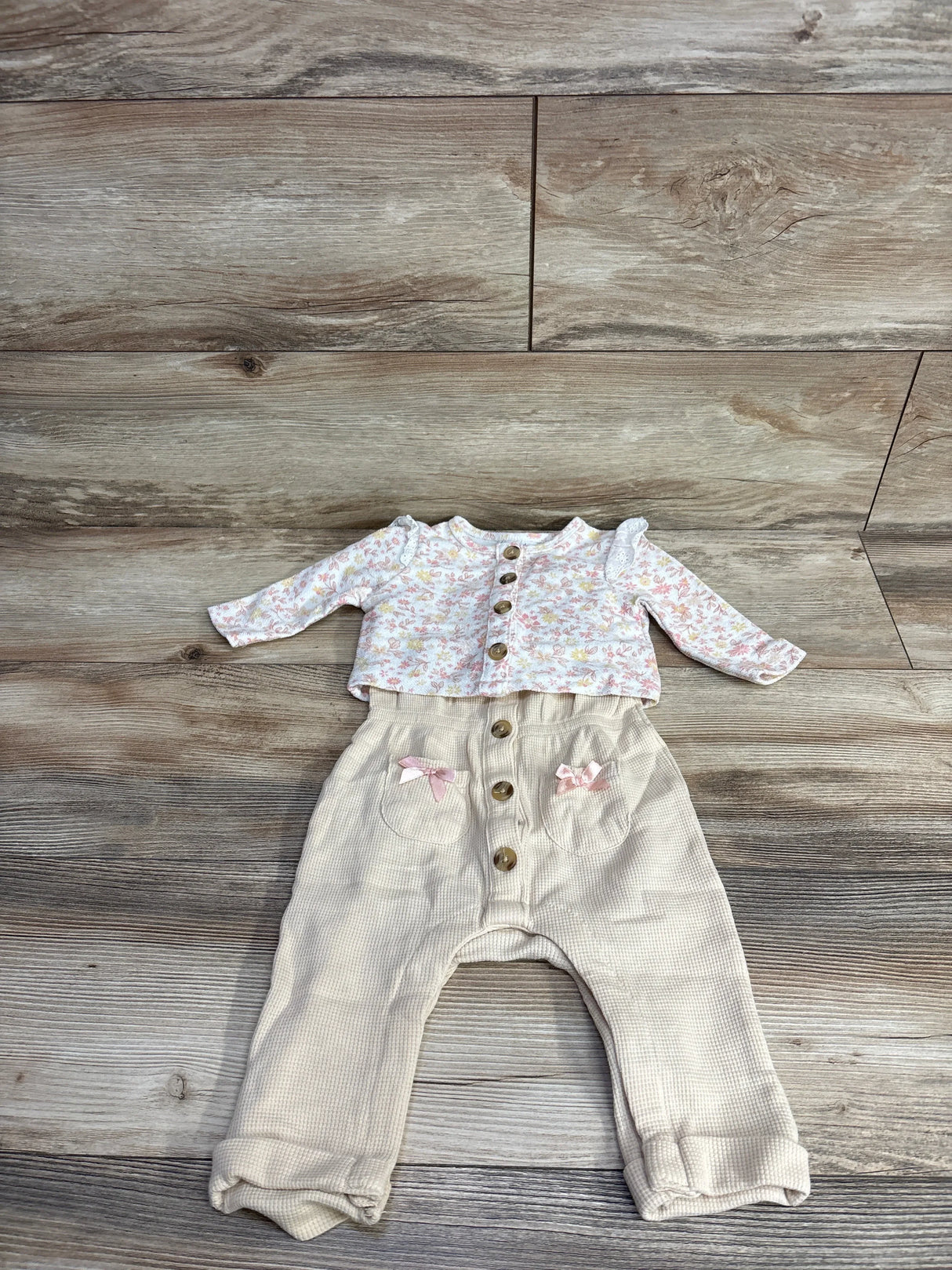 Girls baby outfit with floral long sleeve top and beige button-up pants on wood floor
