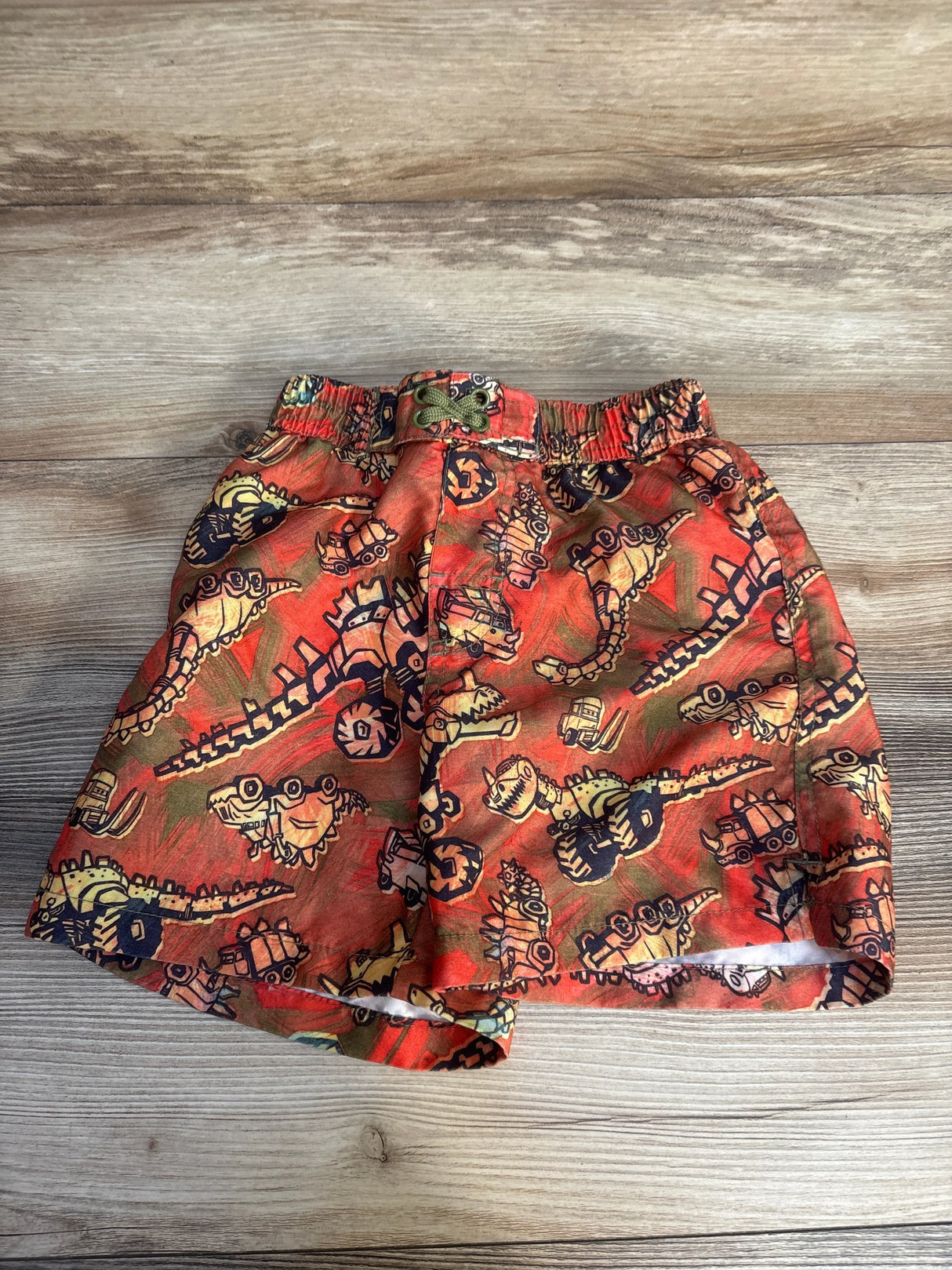 Red boys' shorts with fun dinosaur and vehicle cartoon print on wood background
