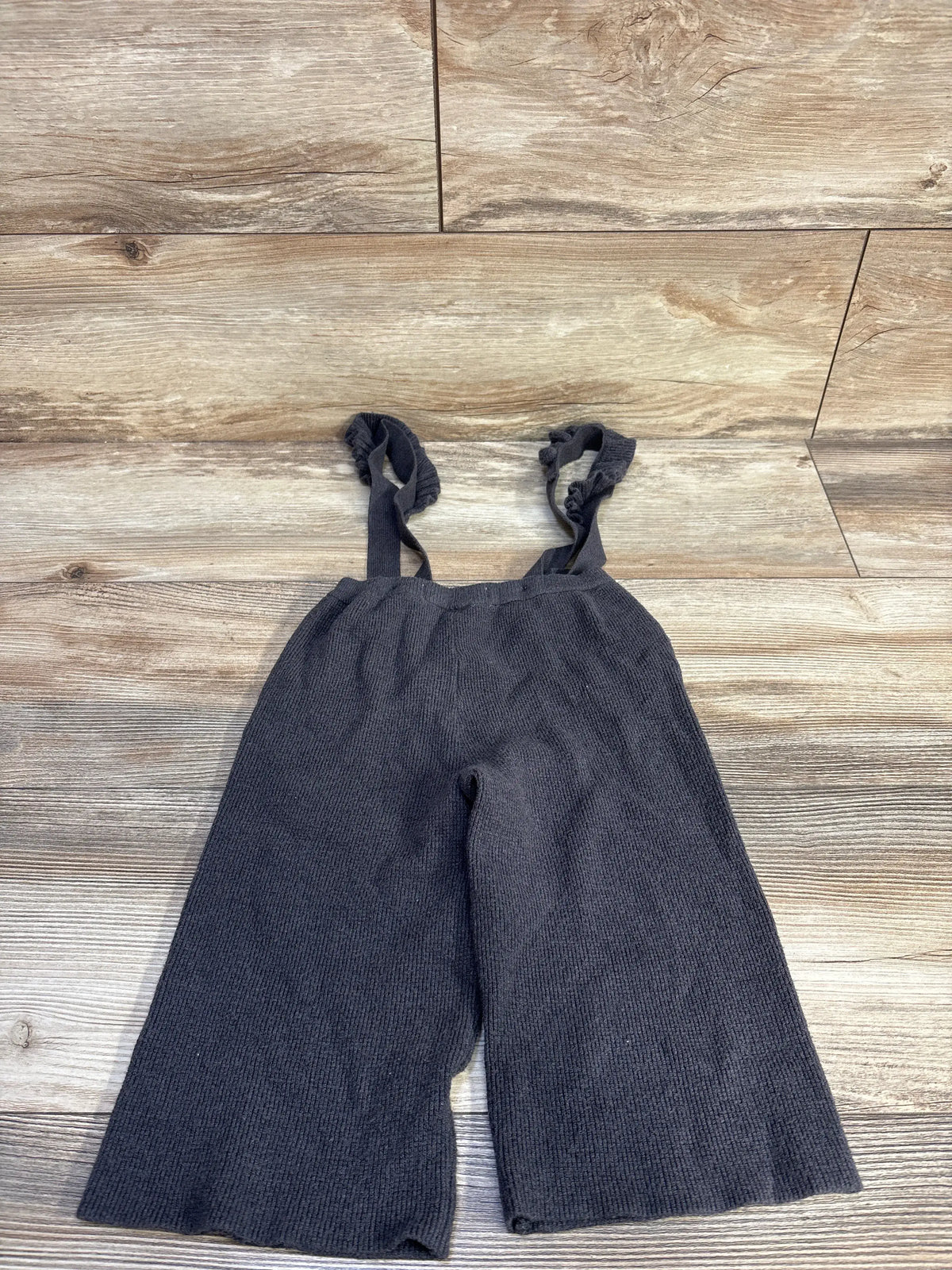 Front view of Zara knit suspender pants in grey for 18 to 24 months, showcasing ribbed knit fabric and suspender straps on wood grain