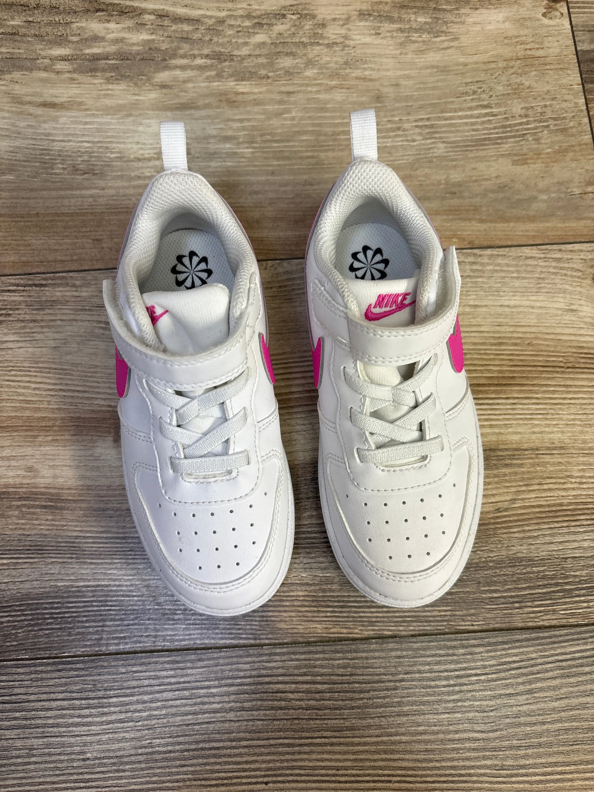 Top view of toddler Nike Court Borough Low Recraft white sneakers showing laser fuchsia Swoosh and Velcro strap on wood floor