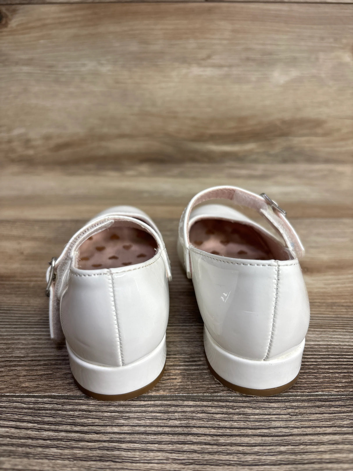 Back view of white patent toddler girl dress shoes with ankle straps on wood floor