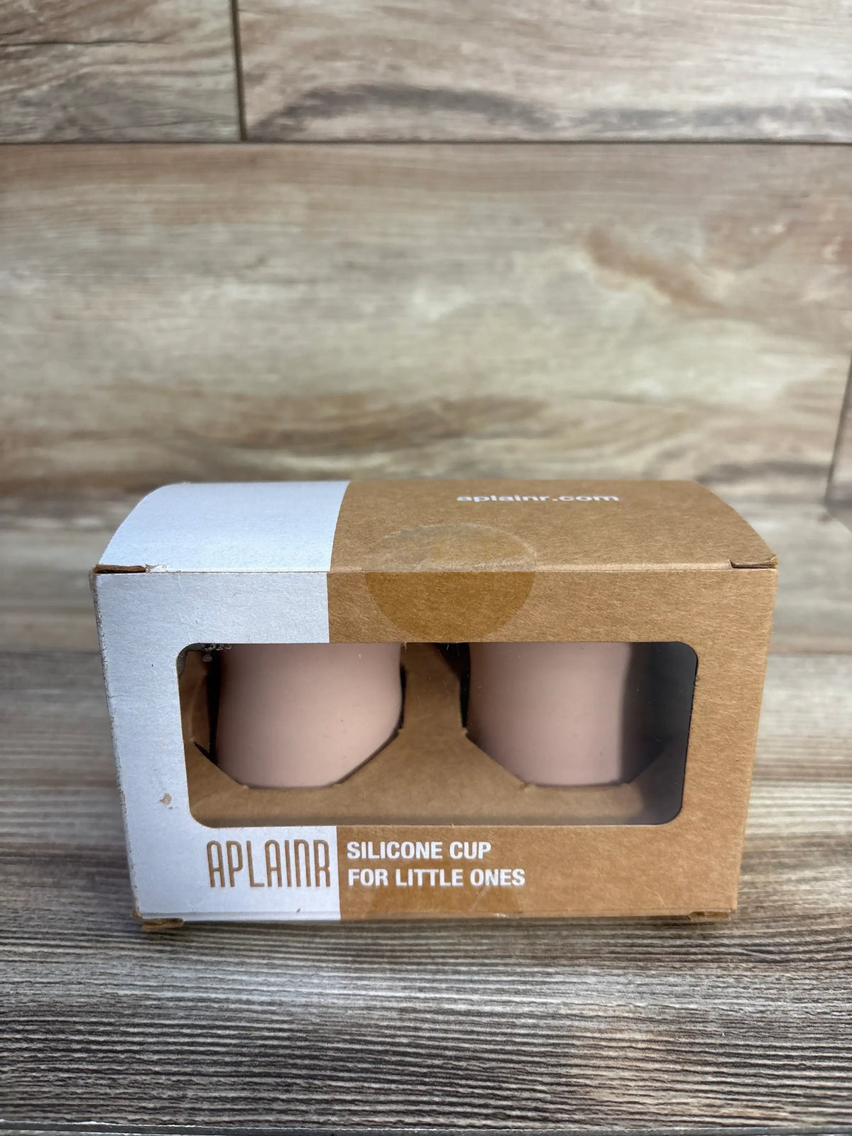 Front view of two pink APLAINR silicone training cups in a windowed cardboard box on a wood surface
