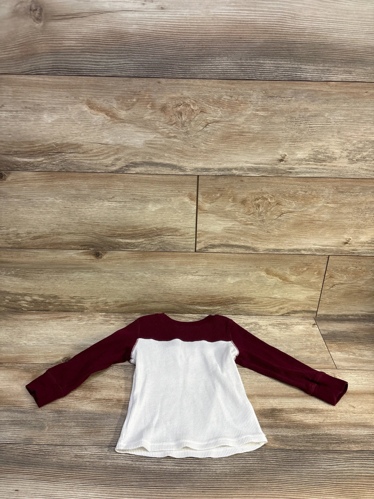 Flat lay of Cat & Jack toddler waffle-knit long sleeve shirt showing maroon sleeves and white textured body on wood background
