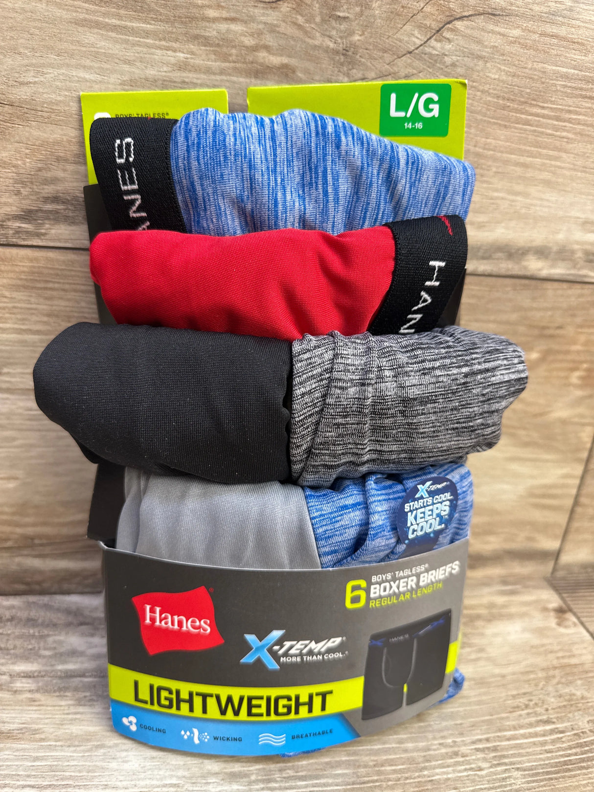 Front view of 6-pack Hanes X-Temp boys’ tagless boxer briefs in assorted colors with LIGHTWEIGHT packaging on wood background