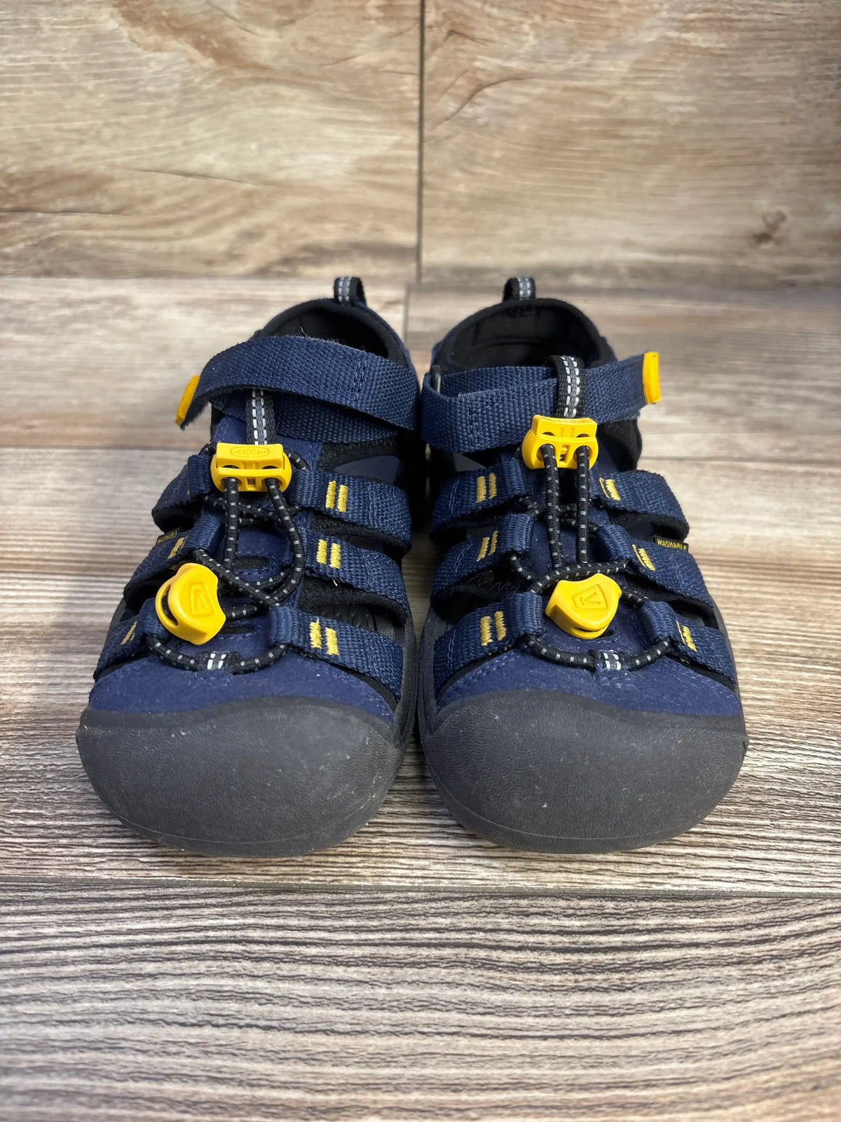 Front view of navy KEEN Newport H2 sandals showcasing yellow toggles and adjustable straps on a wood surface