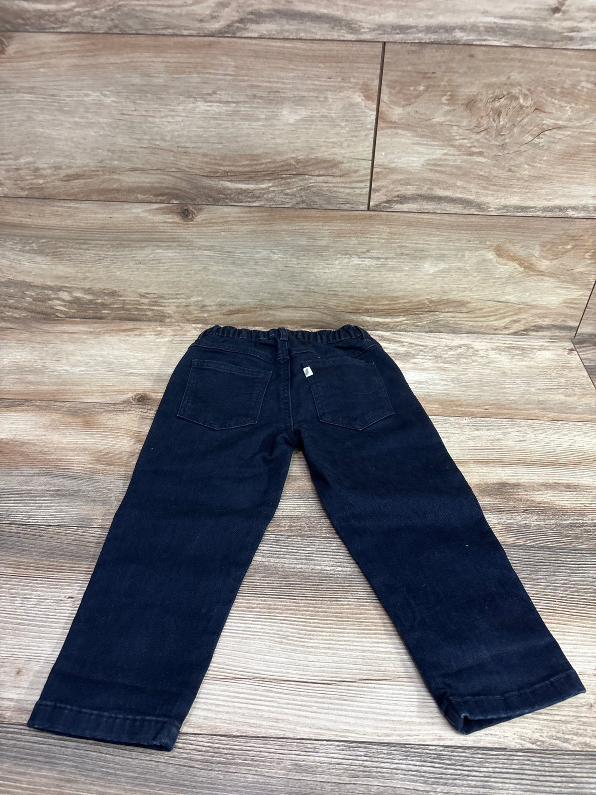 Back view of Easy Peasy dark wash navy blue jeans for toddlers, size 3T, on a wood background.