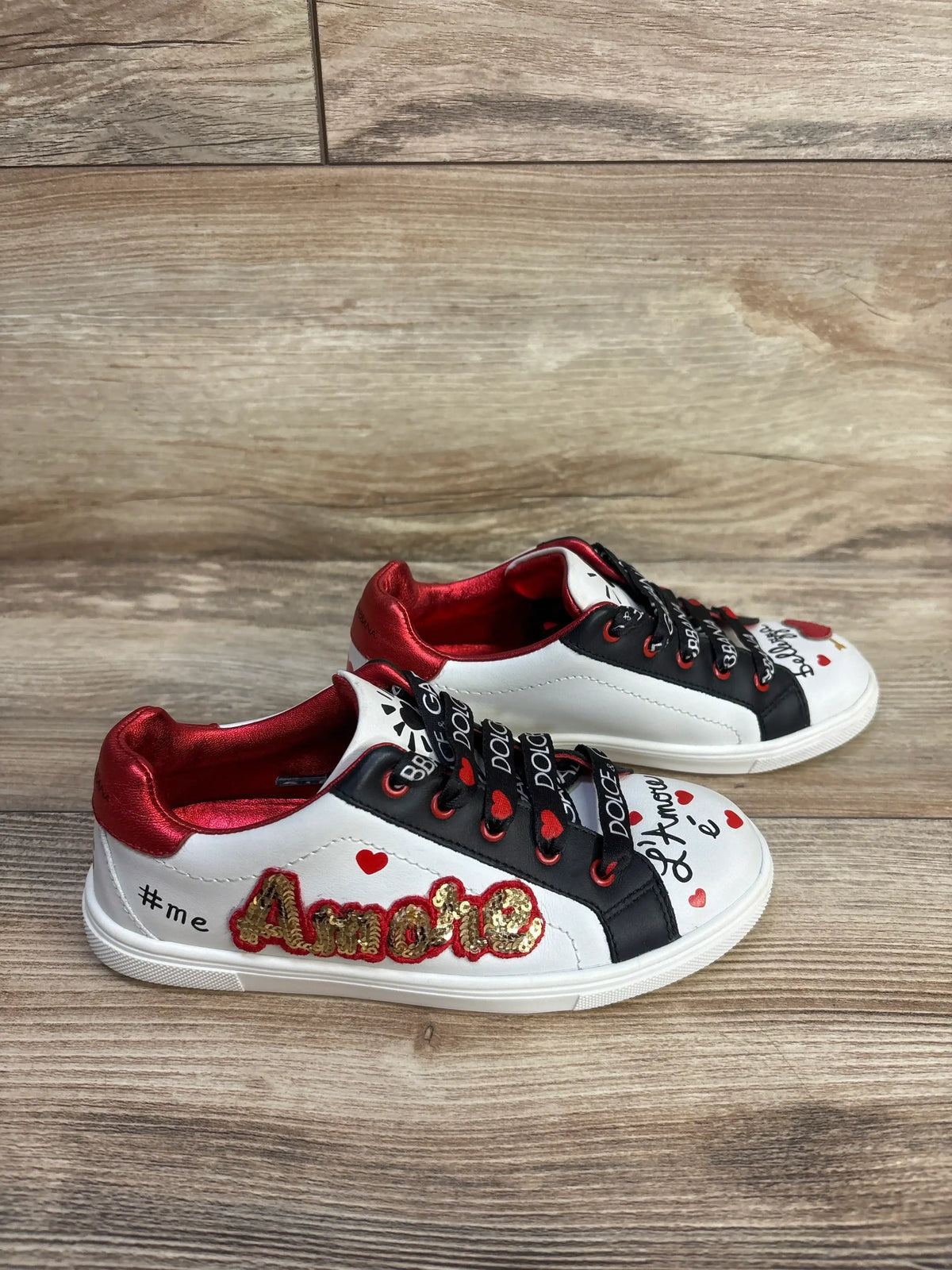 Angled view of white Portofino DG Amore calfskin sneakers showcasing red hearts and gold embellishment on a wood floor