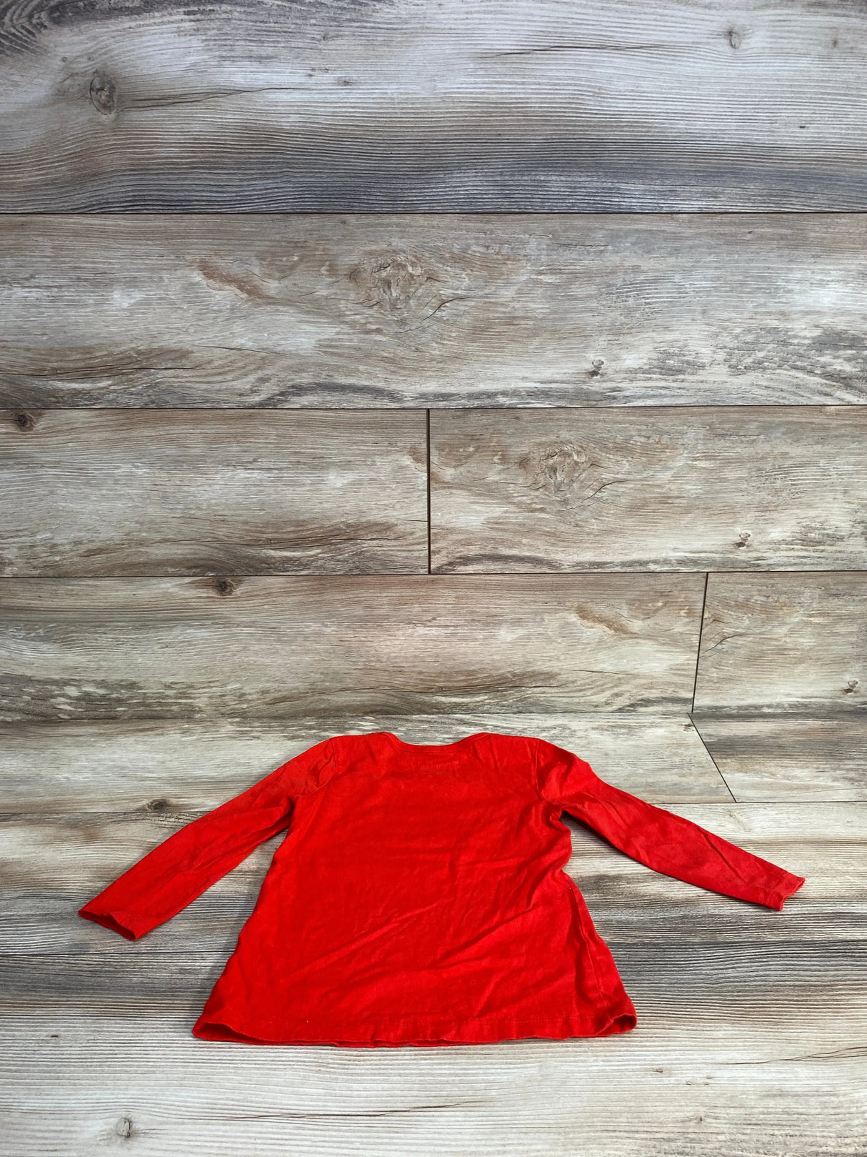 Red long sleeve toddler shirt displayed on rustic wood background