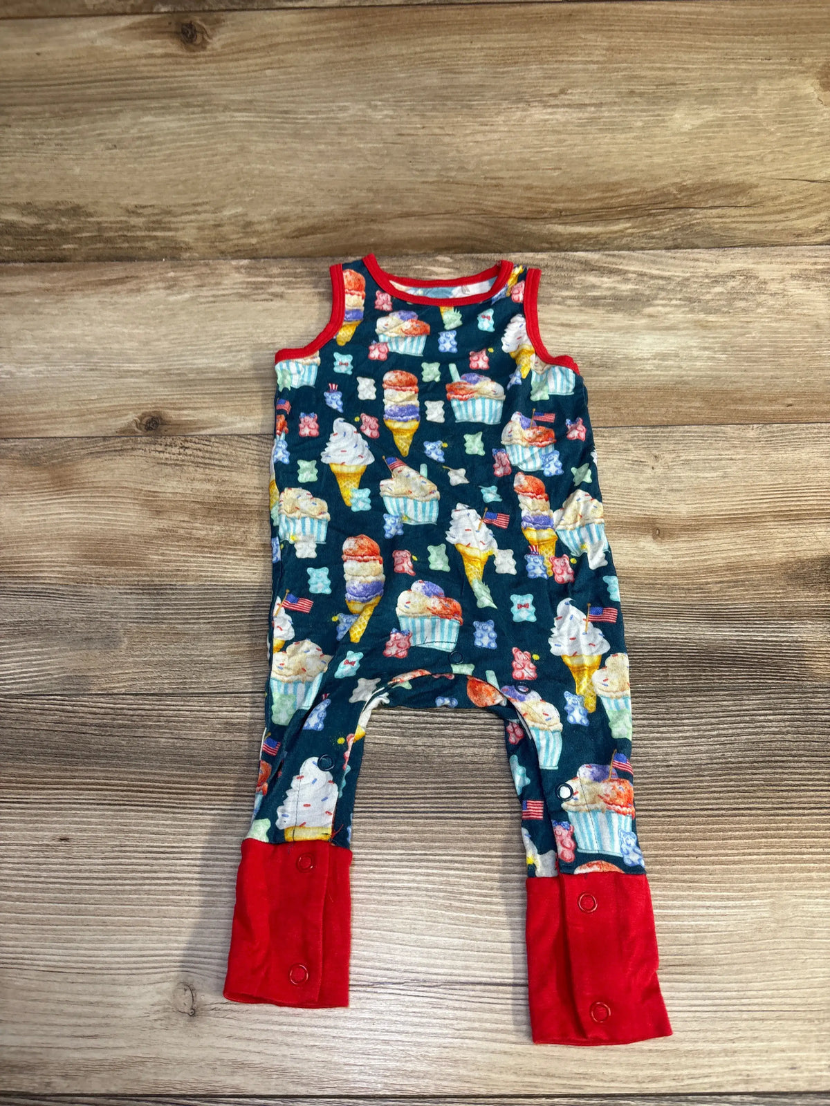 Front view of blue Posh P. bamboo sleeveless jumpsuit, size 3-6m, showcasing treat print and red trim on wood background