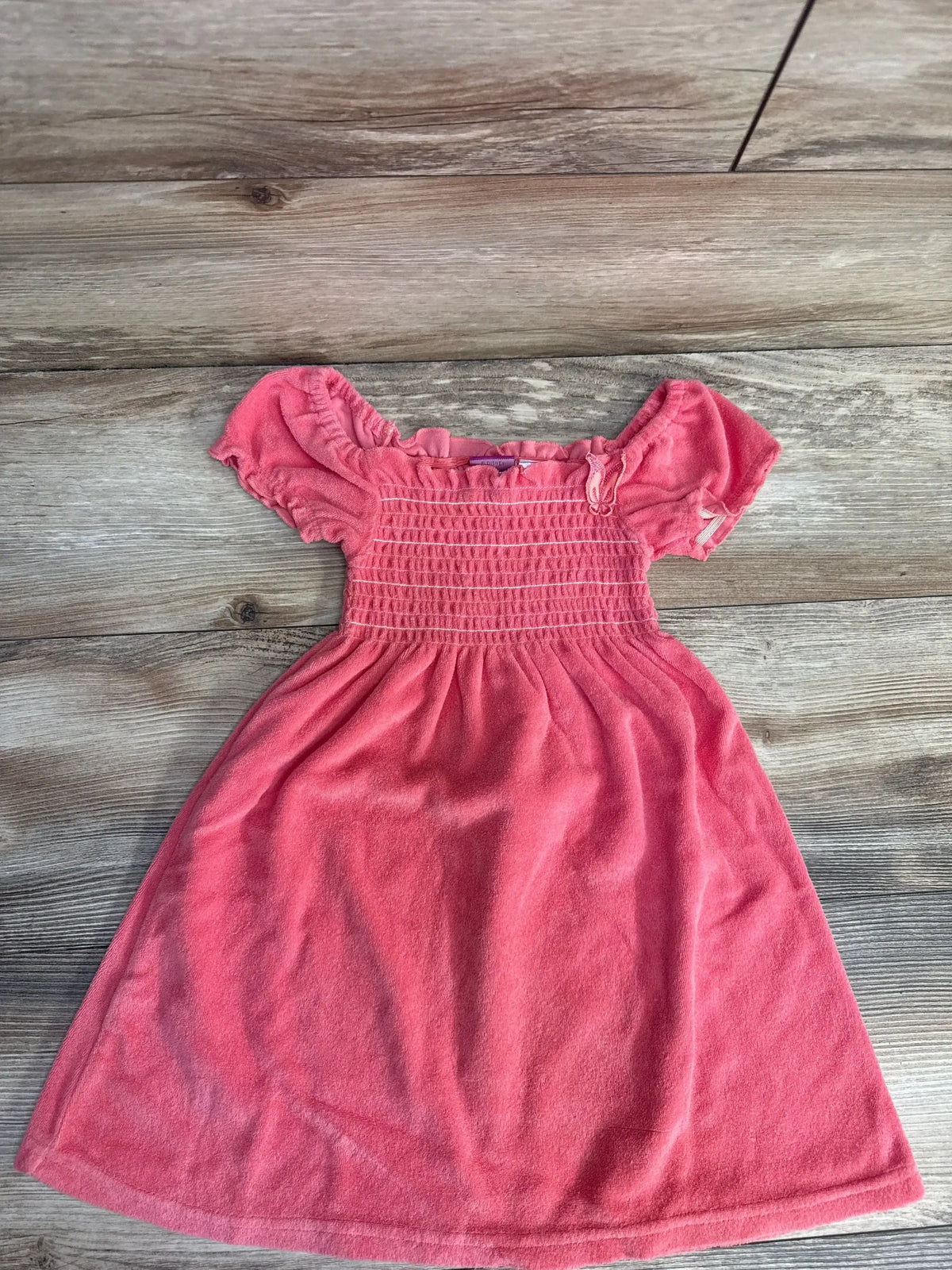 Flat lay of Disney Princess Smocked Terry Cloth Swim Cover Dress in coral red showcasing puff sleeves and smocked bodice with wood plank background