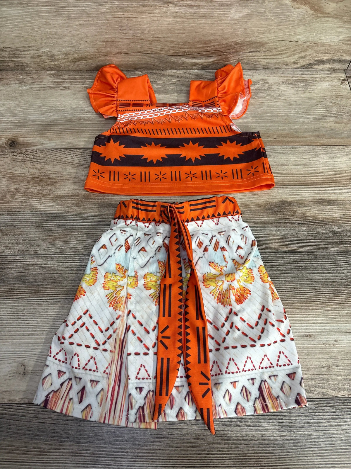 Flat lay of 2pc tank and skirt set in orange with Moana inspired tribal print top and skirt with sash tie on wood plank floor