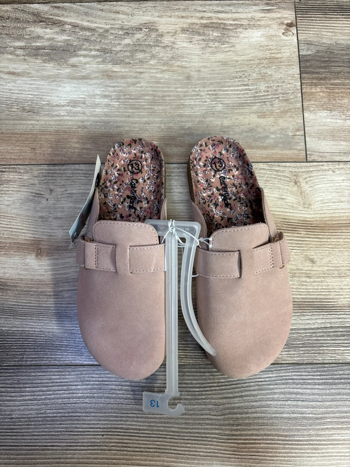 Pair of pink toddler slip-on shoes with floral print insoles on wooden floor