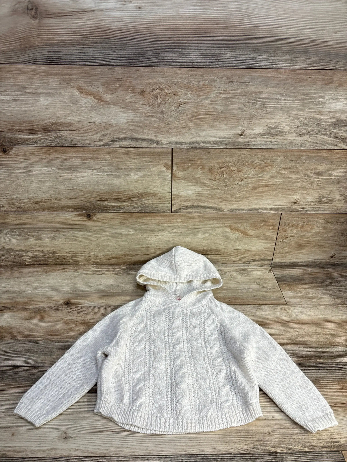 White knitted hooded sweater with cable patterns on wooden background