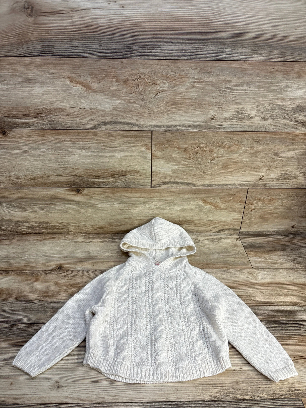 White knitted hooded sweater with cable patterns on wooden background