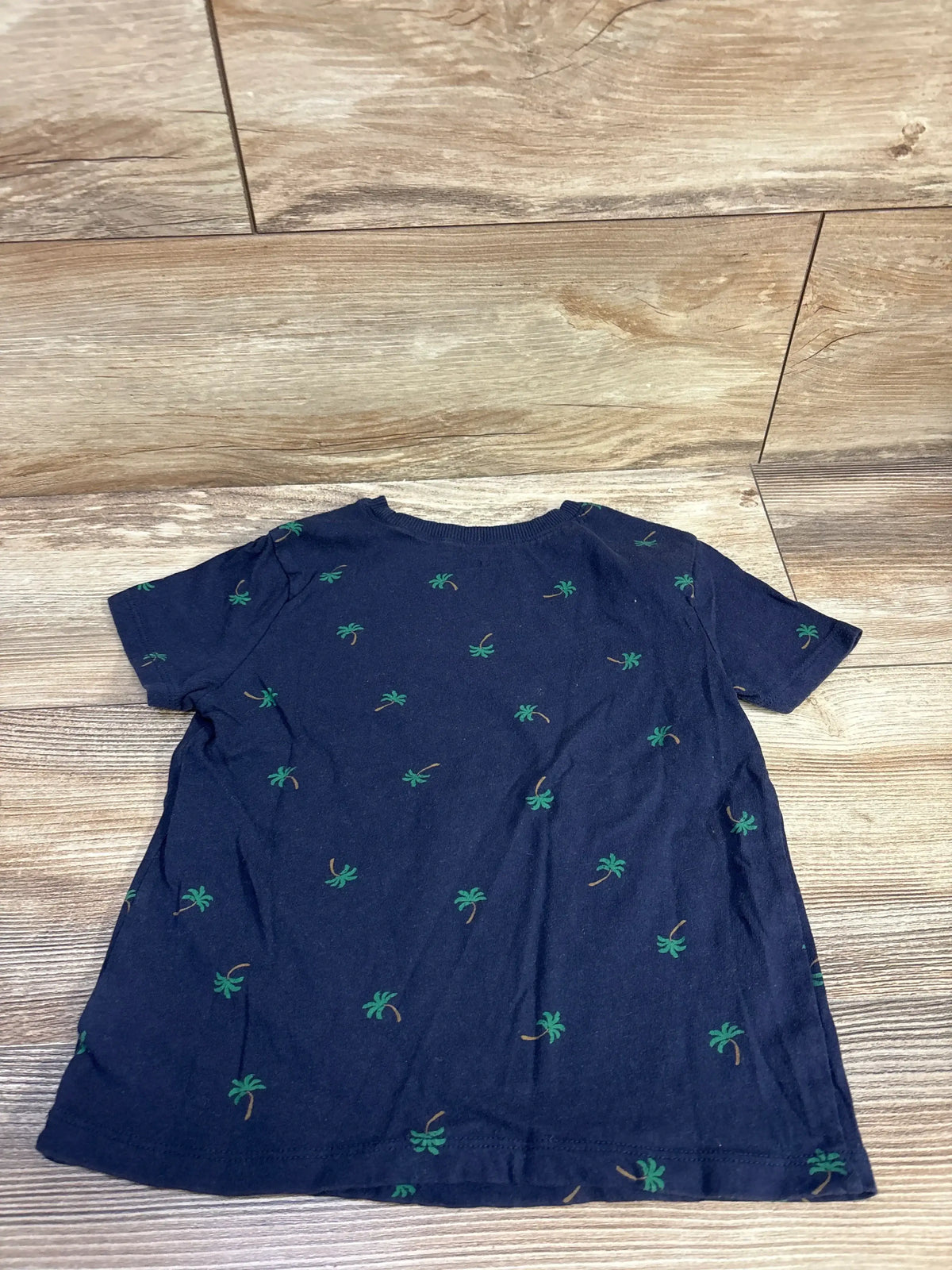 Back view of Old Navy navy toddler t-shirt showcasing all-over green palm tree print and short sleeves, laid flat on a wood floor