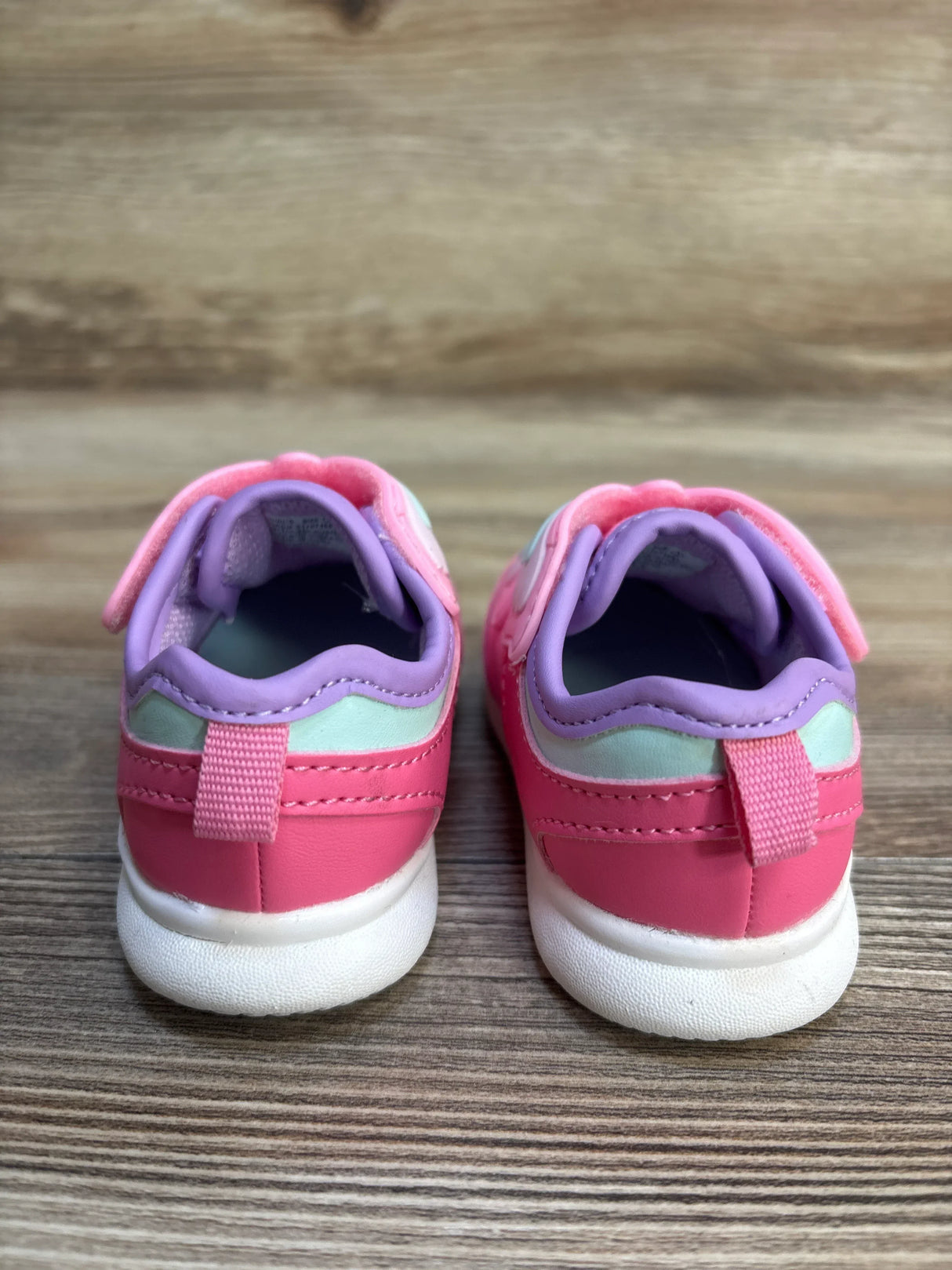 Rear view of Just One You Butterfly light-up sneakers size 3C showing pink and purple uppers, pull tabs and white soles on wooden surface