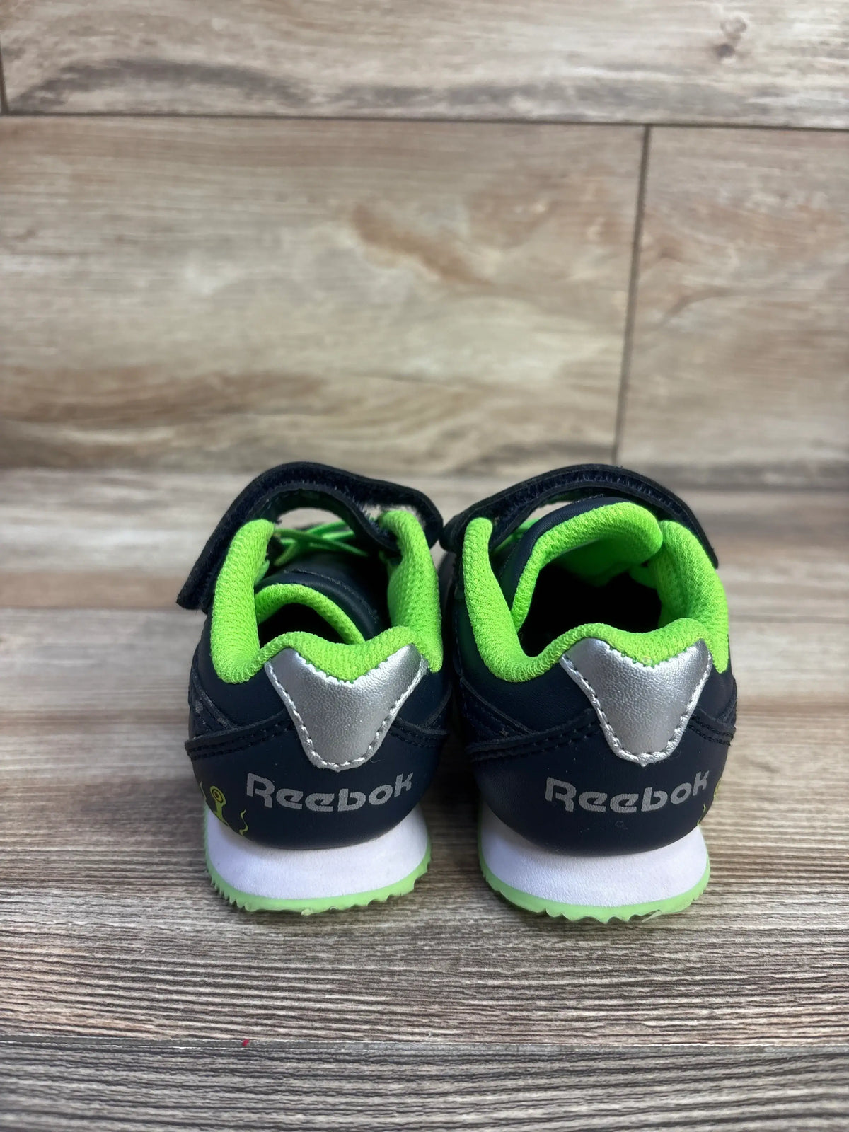 Rear view of Reebok Space Sneakers Navy/Green sz 6c showcasing hook and loop closures with a wood-look floor background