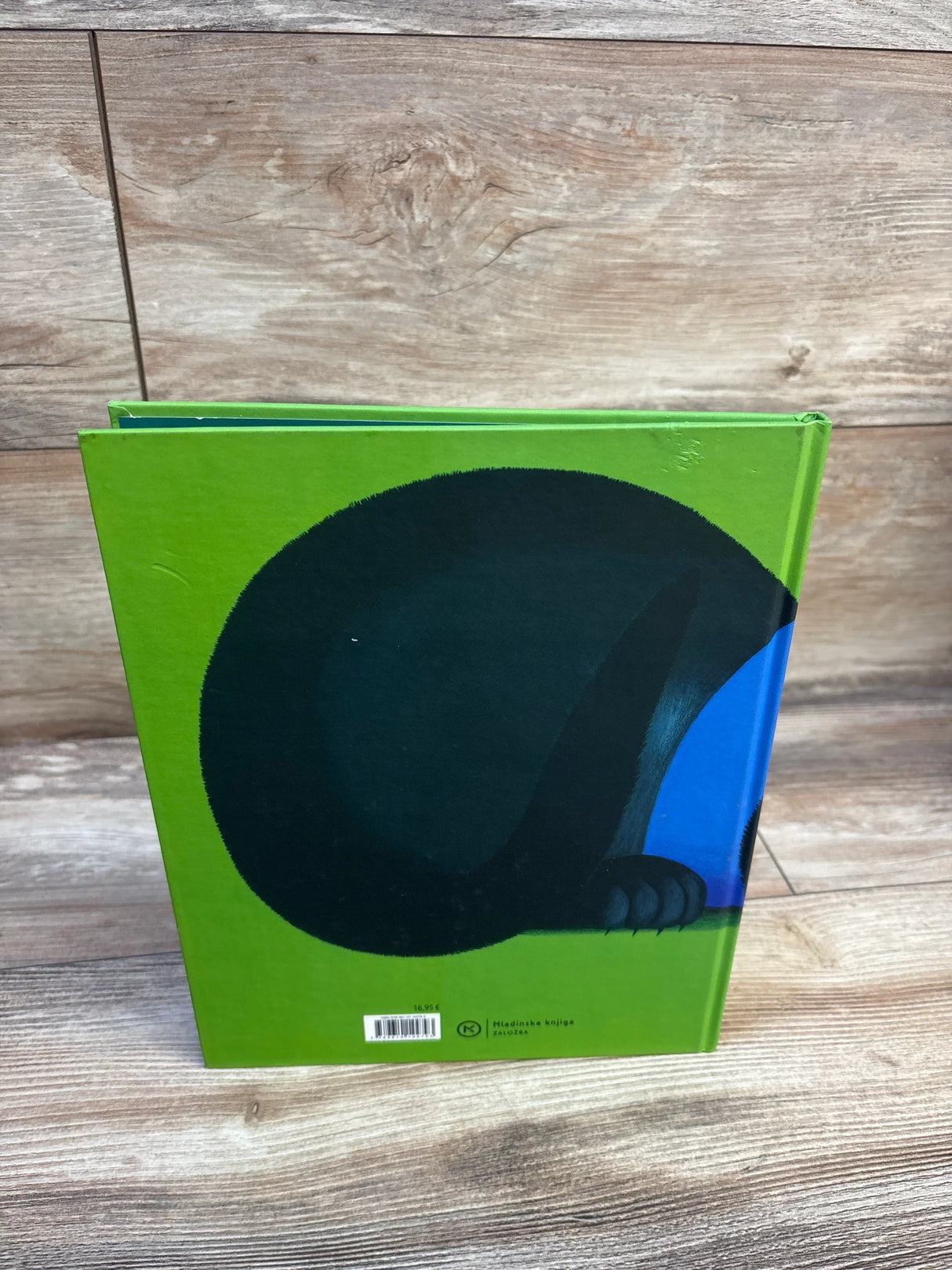 Bright green children's book with black dinosaur illustration on wooden surface
