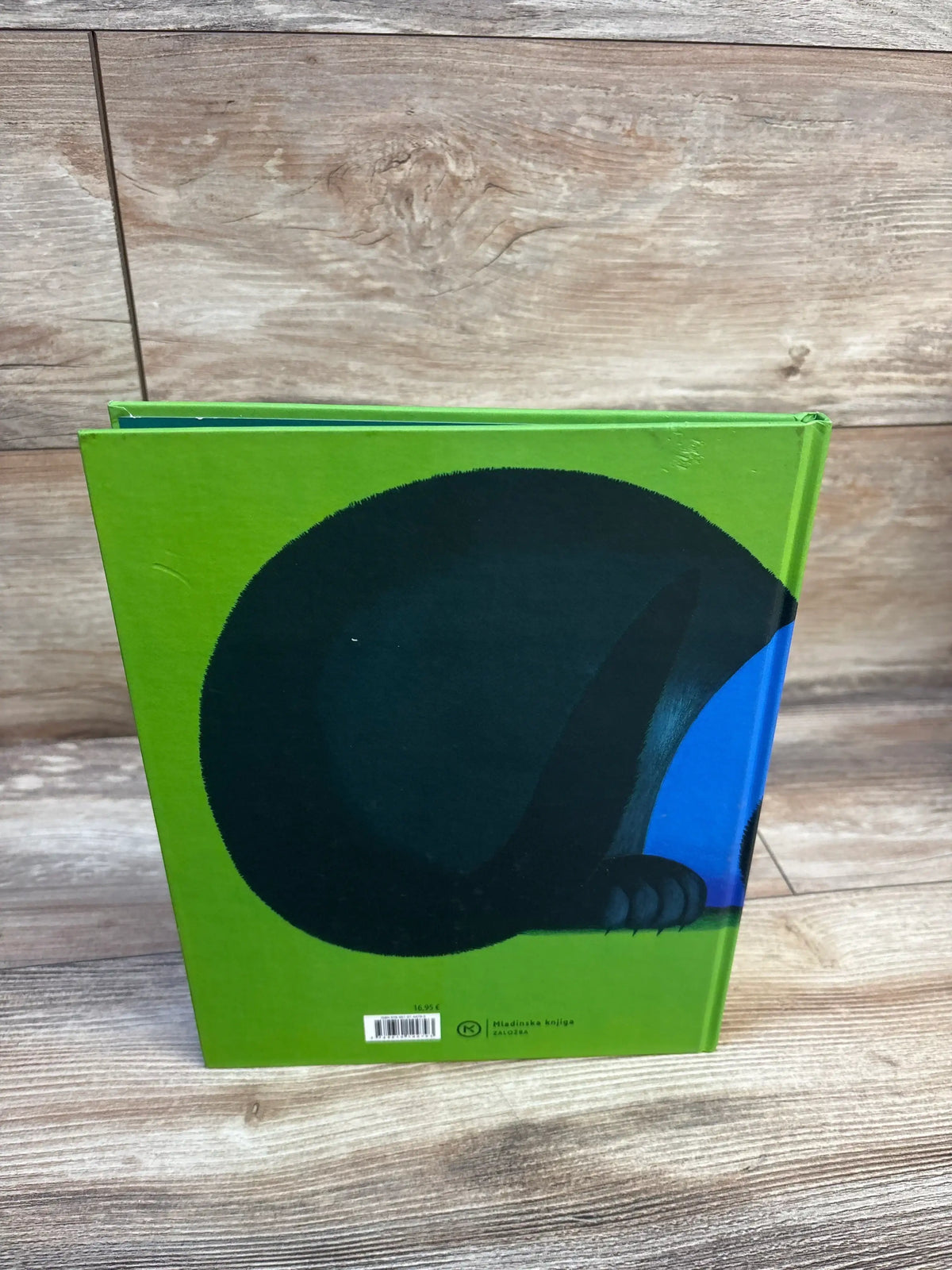 Back of Magic Muri hardcover book showing large black animal illustration with blue paw on green cover on wooden surface