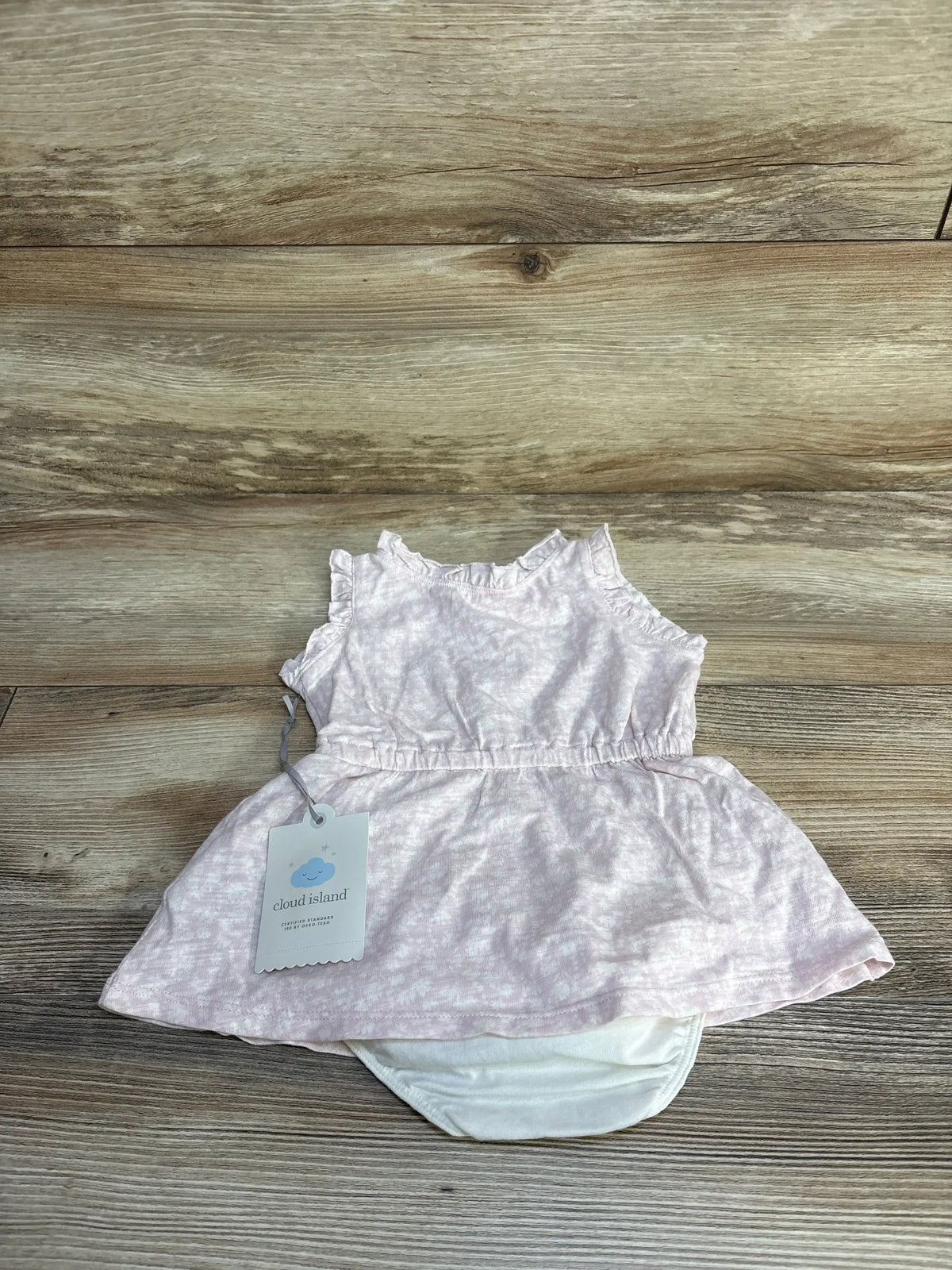 Flat lay of newborn Cloud Island floral-print off-white dress with attached diaper cover on wood floor