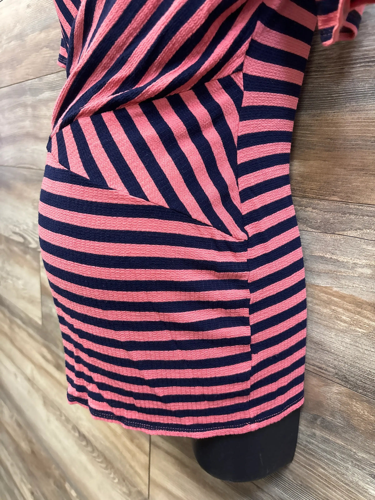 Close-up view of Motherhood Maternity coral striped nursing top showcasing overlapping nursing panel on wood-look flooring