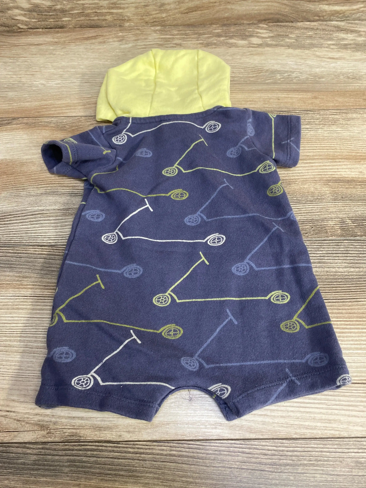 Flat-lay back view of hooded henley romper showcasing navy fabric with scooter print and yellow hood on wood background