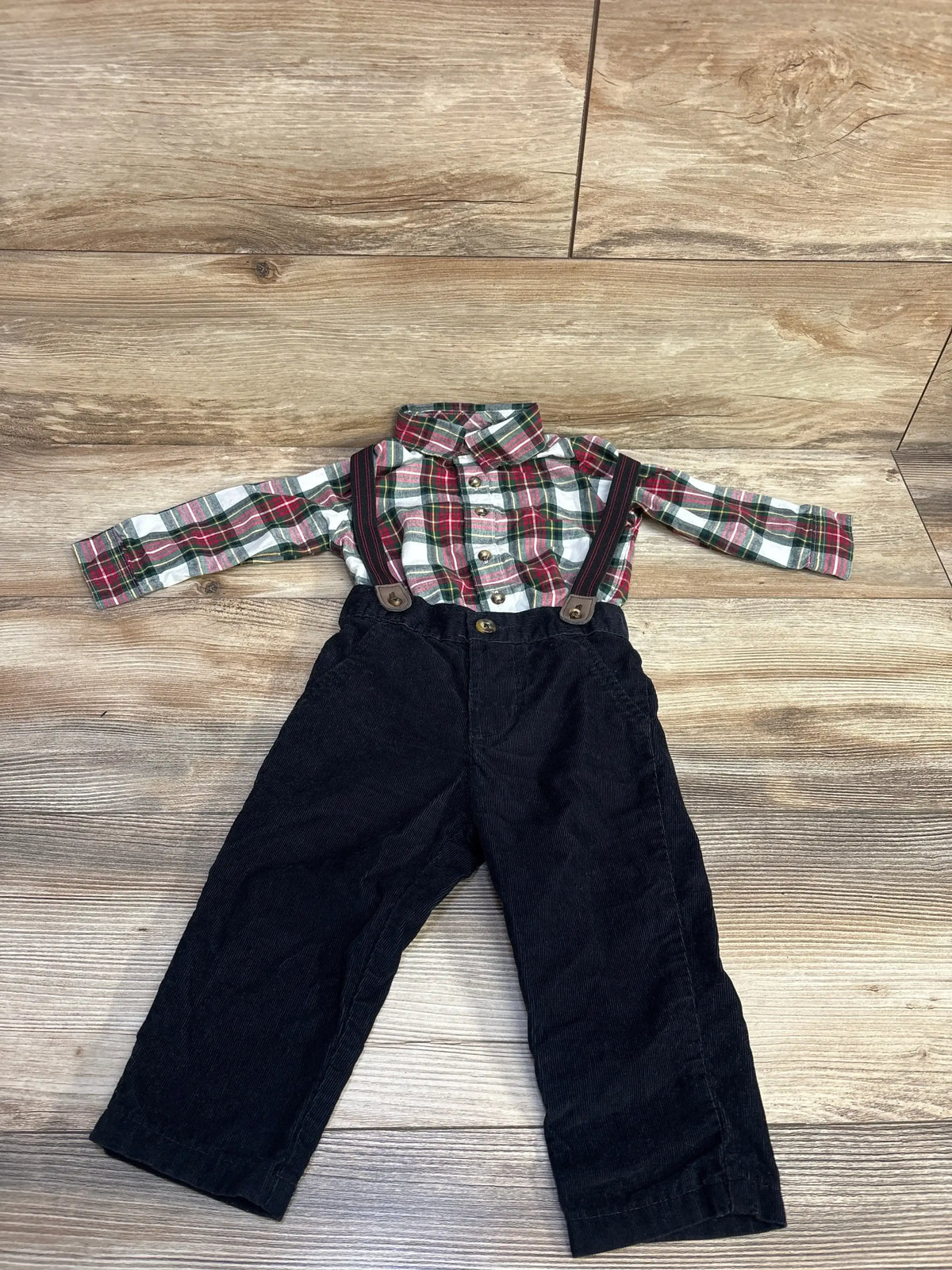 Toddler outfit with red and green plaid shirt and black corduroy pants with suspenders on wood floor
