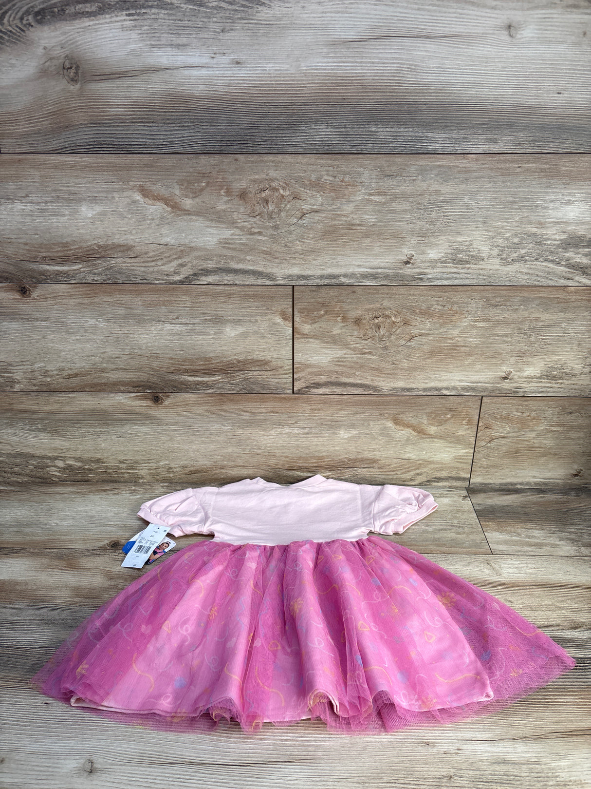 Flat lay of pink toddler tulle dress size 2T showing puff sleeves and layered tulle skirt on wood plank background