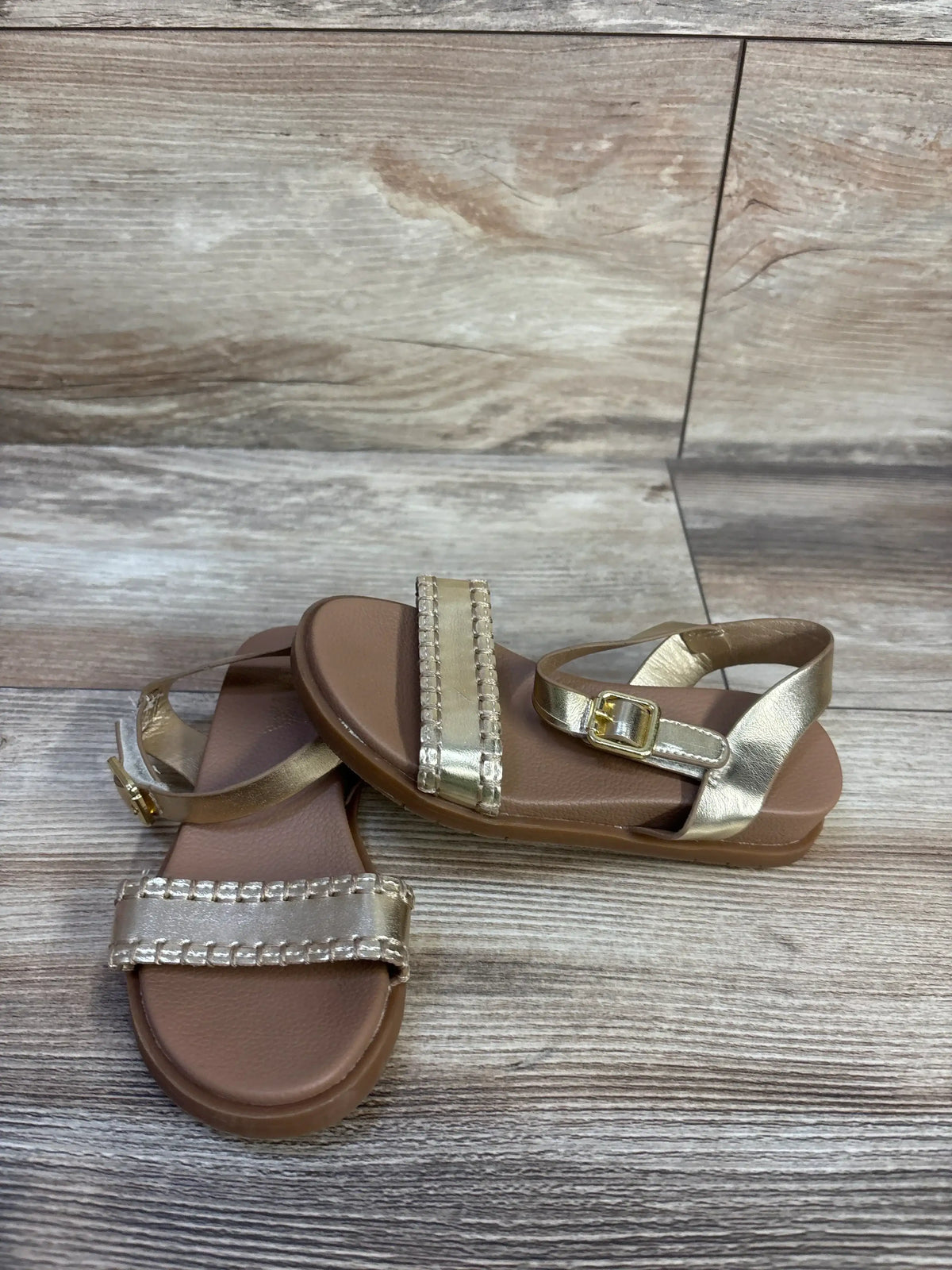 Angled top view of MIA Peyton sandal (toddler) in metallic gold, showing jeweled front strap and ankle buckle on wood floor