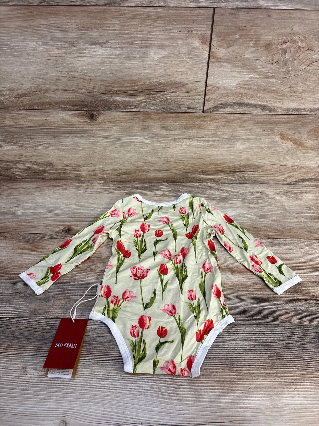 Floral tulip print baby onesie with long sleeves, soft fabric, and brand tag on wooden floor