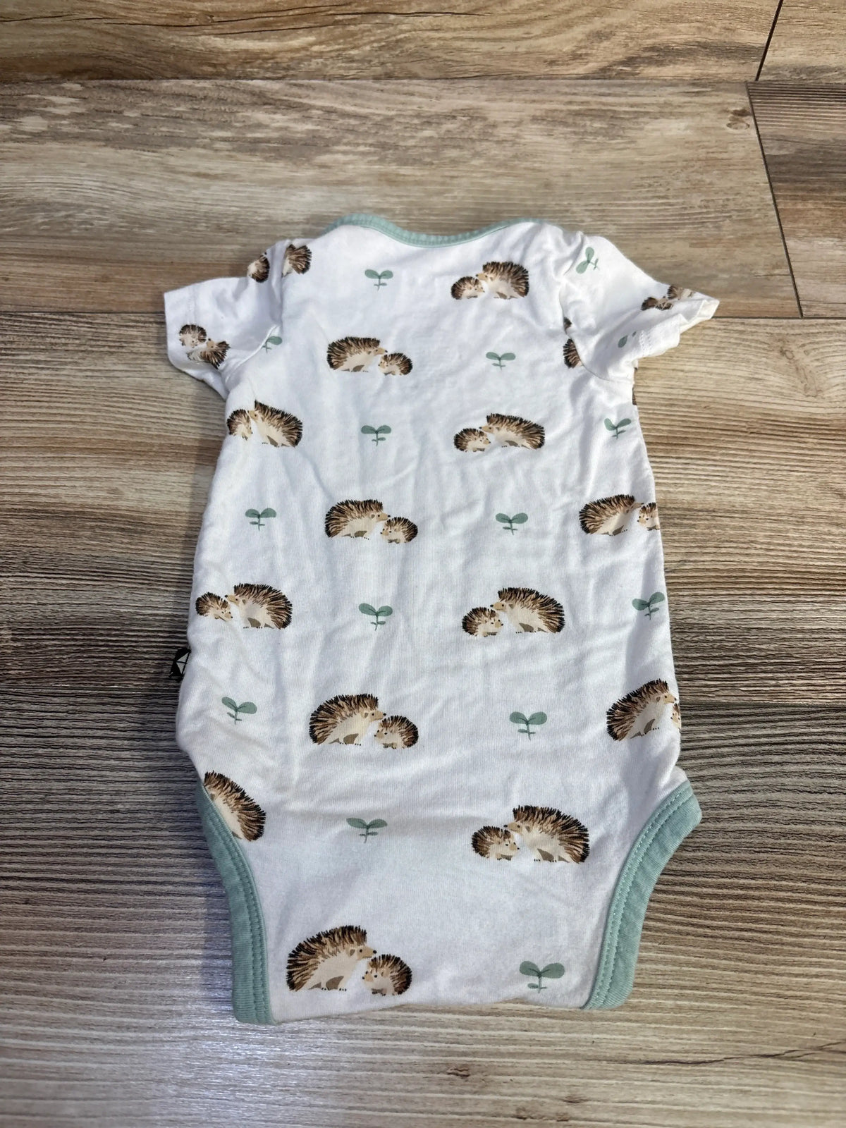 Front view of Kyte Baby bodysuit in Hedgehog White showcasing hedgehog print and short sleeves on a wood floor