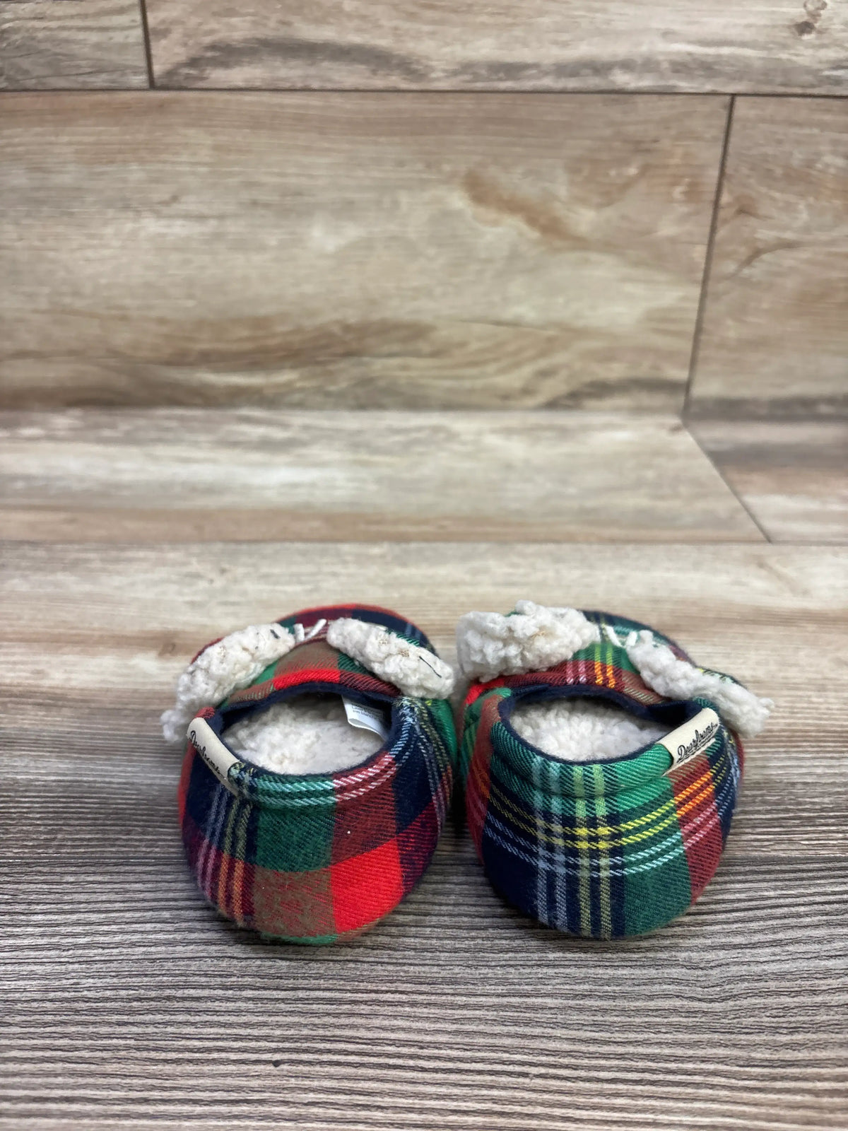 Front view of Dearfoams Baby Bear Slippers, size 4C, showcasing multicolor plaid fabric and sherpa lining on a wood-look floor