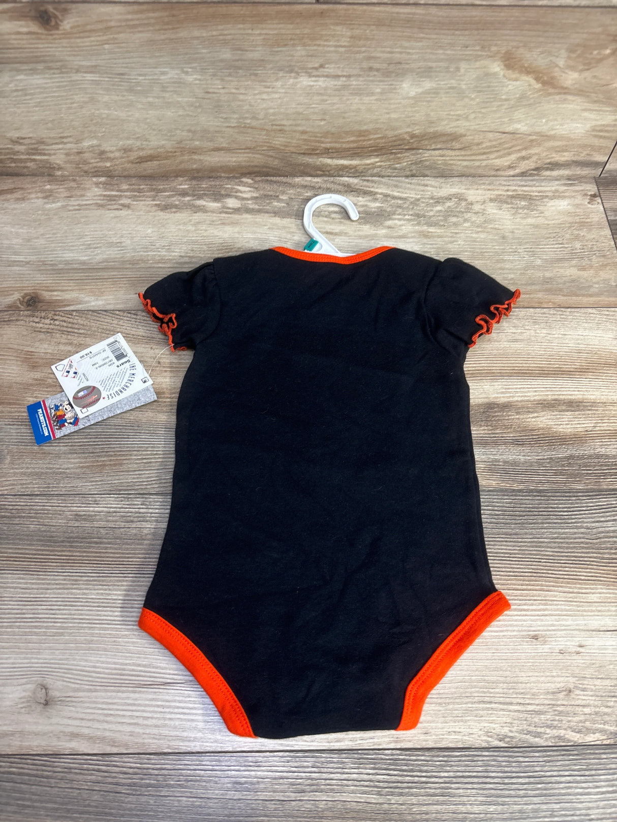 Black baby onesie with orange trim on wooden floor, displayed on hanger with product tag.