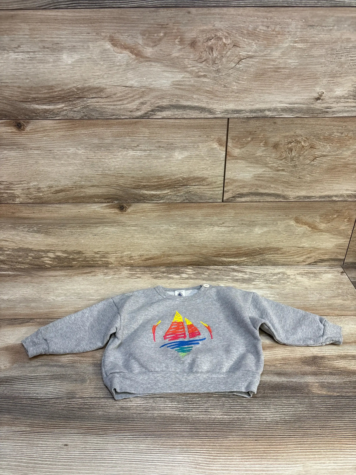 Gray kids sweatshirt with colorful sailboat graphic, laid flat on wood background