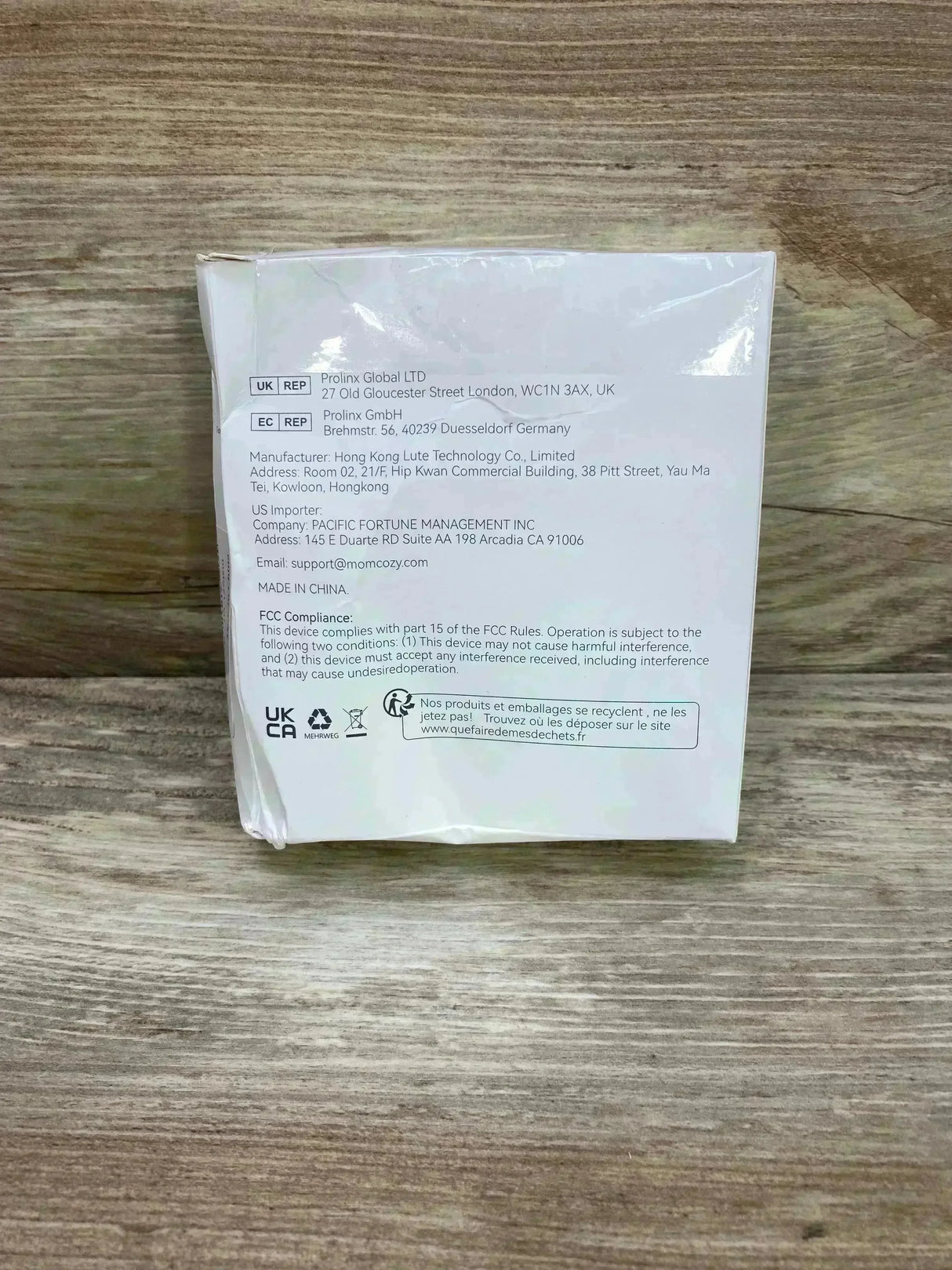 Rear view of Momcozy double sealed flange 27 mm box showing manufacturer info, FCC compliance text and certification icons on a wood surface