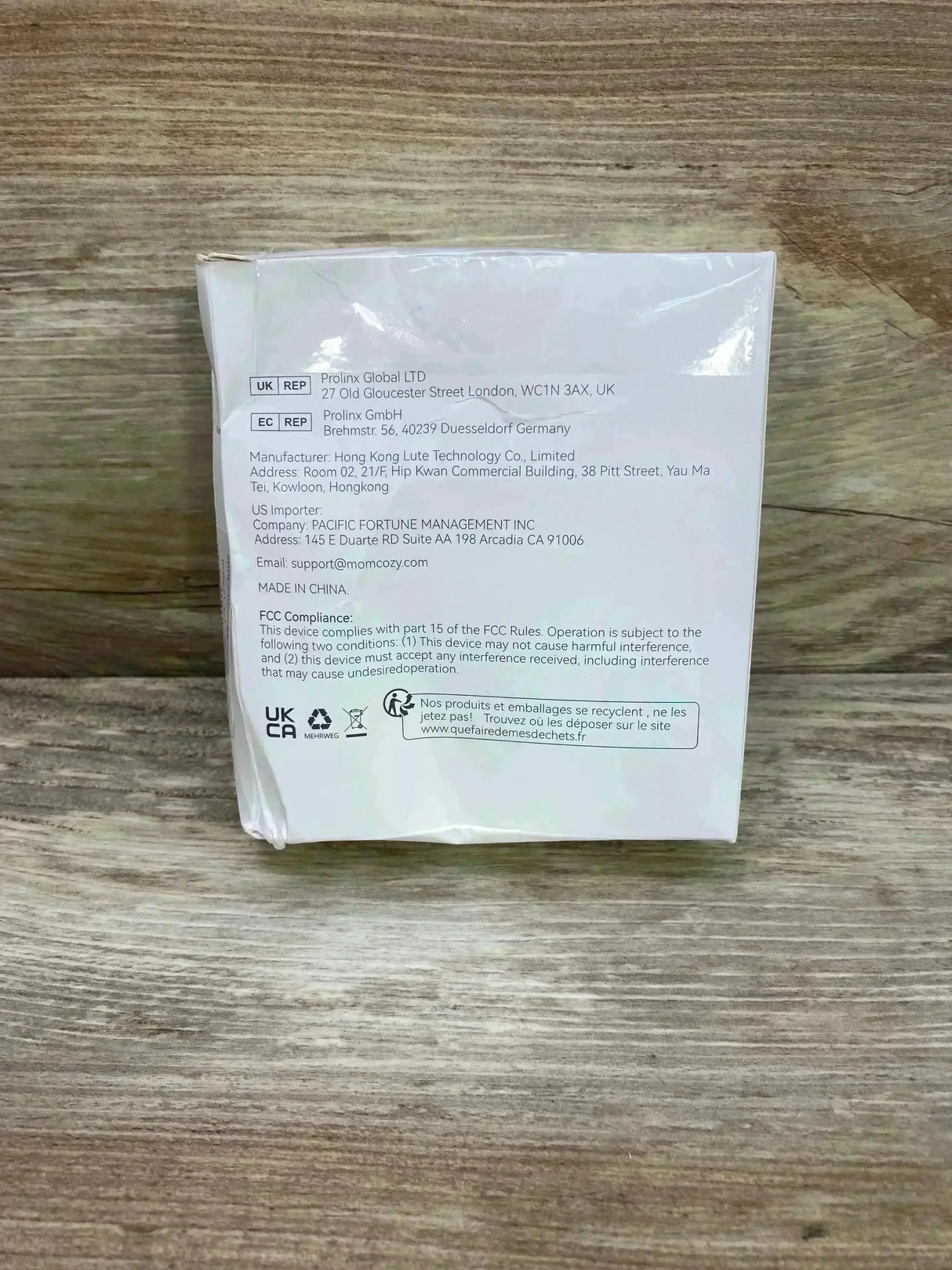 Rear view of Momcozy double sealed flange 27 mm box showing manufacturer info, FCC compliance text and certification icons on a wood surface
